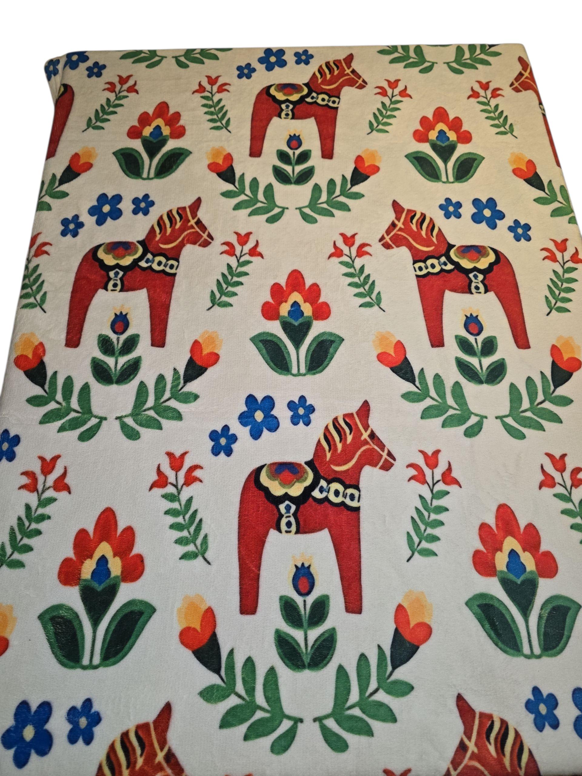 Inspired by Swedish heritage, the Blanket: Dala Horse Children's Blanket 29" x 40" features red decorative horses and vibrant flowers on a white background, echoing classic Dala Horse designs.