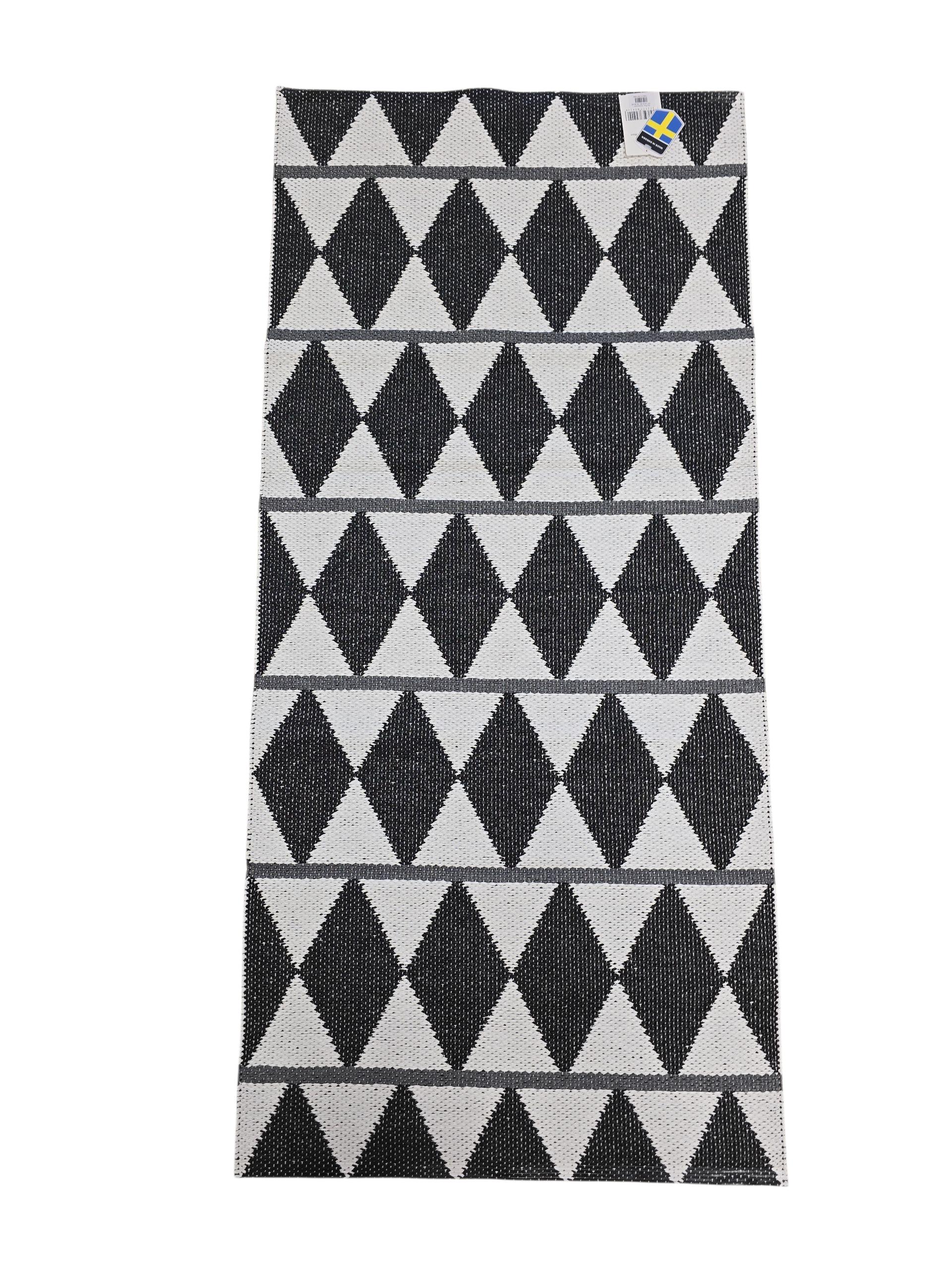 The Vinyl Rug: Horredsmattan - Zigge features a rectangular woven design with a black and white geometric diamond pattern, gray stripes on one side, and a small corner tag.