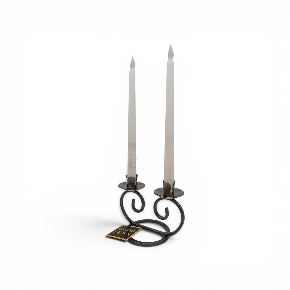 The Talla Imports Candle Holder: Danish Iron Double Curls holds two white taper candles in curled black iron arms, with a small rectangular tag attached. The holder is hand forged and set against a plain white background.