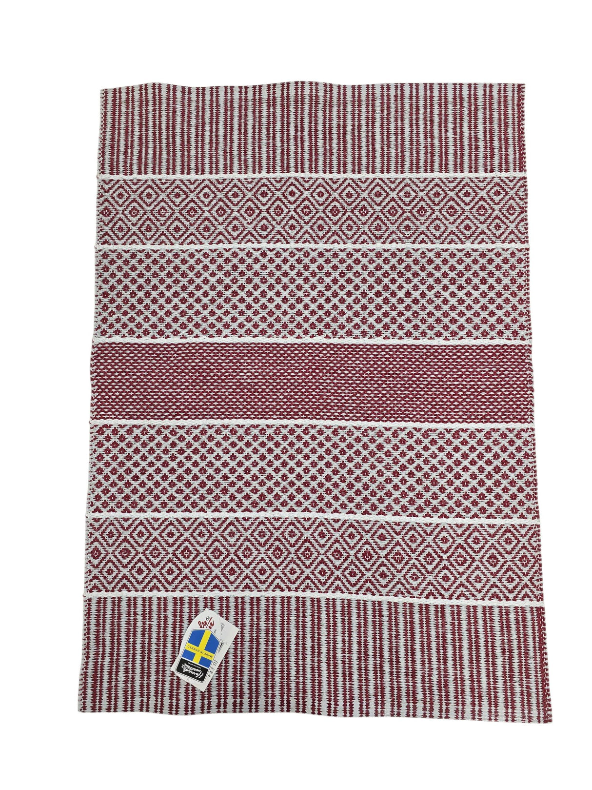 The Vinyl Rug: Horredsmattan - Alfie - Red is a rectangular Swedish vinyl rug featuring red and white geometric patterns and a corner tag with the Swedish flag.