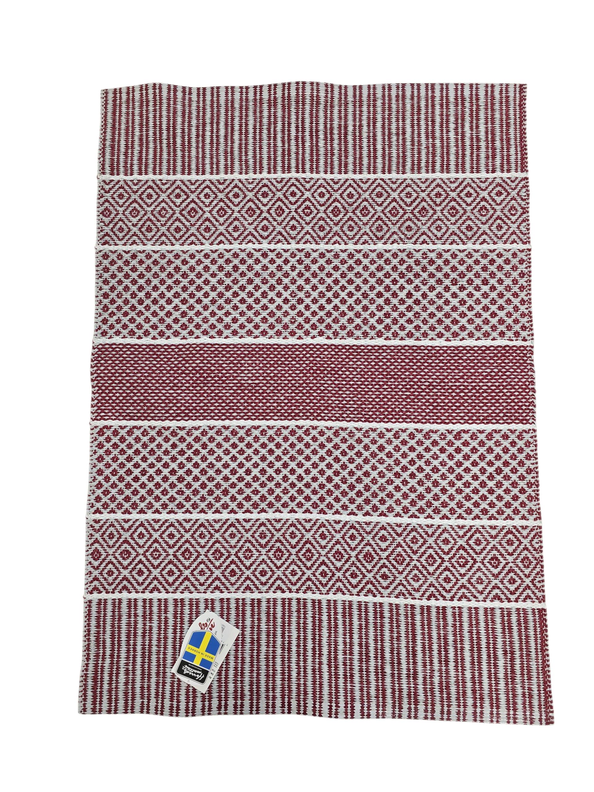 The Vinyl Rug: Horredsmattan - Alfie - Red is a rectangular Swedish vinyl rug featuring red and white geometric patterns and a corner tag with the Swedish flag.