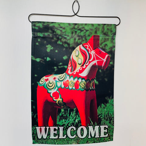 A small polyester garden flag featuring a red Swedish Dala horse in the forest with Welcome at the bottom.