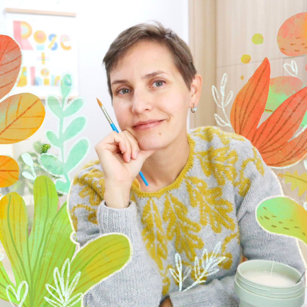 A person smiles while holding a paintbrush amidst illustrated plant motifs, wearing a sweater with a yellow pattern that complements the serene vibe of assembling the 500-piece PuzzleTwist: Scandinavia Map by Mirk Hokkanen.