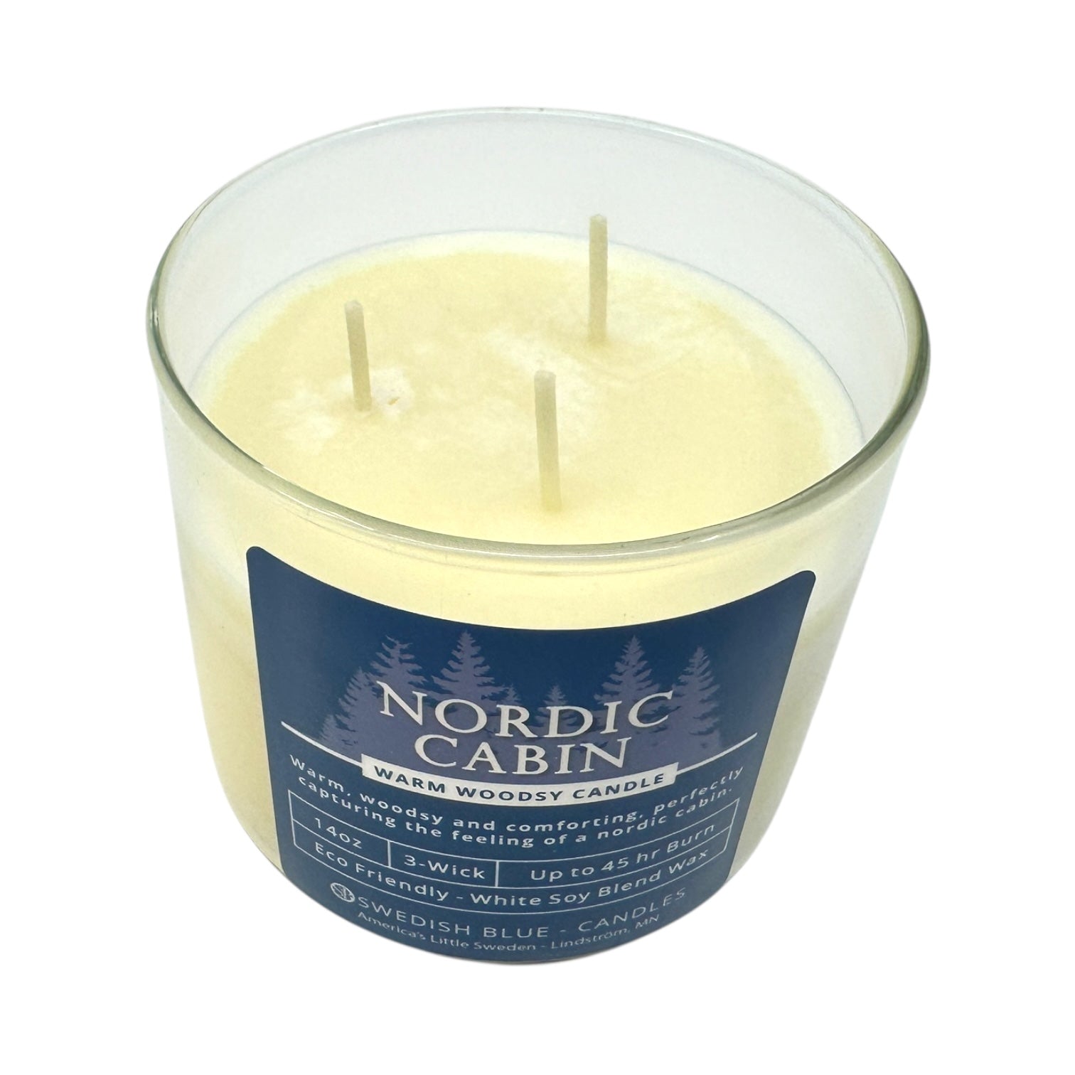 The Candle: Nordic Cabin - Warm Woodsy Candle features pale yellow wax in a glass jar with three unlit wicks. Its eco-friendly white soy blend delivers a forest scent inspired by cozy cabins.