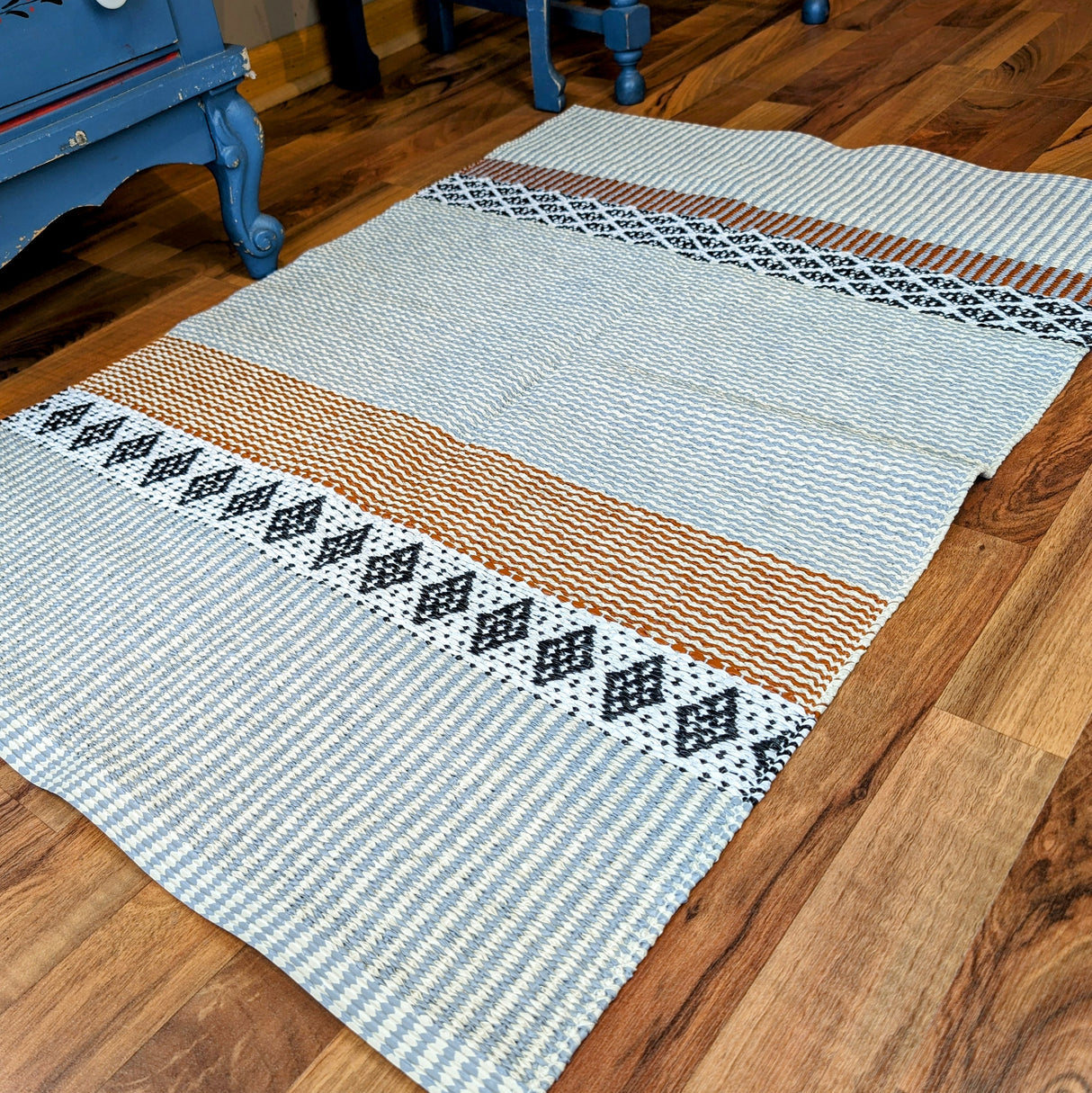 A Horredsmattan Swedish vinyl rug named "Savanne Light Grey" lies elegantly on a wooden floor, offering both style and durability with its subtle geometric patterns.