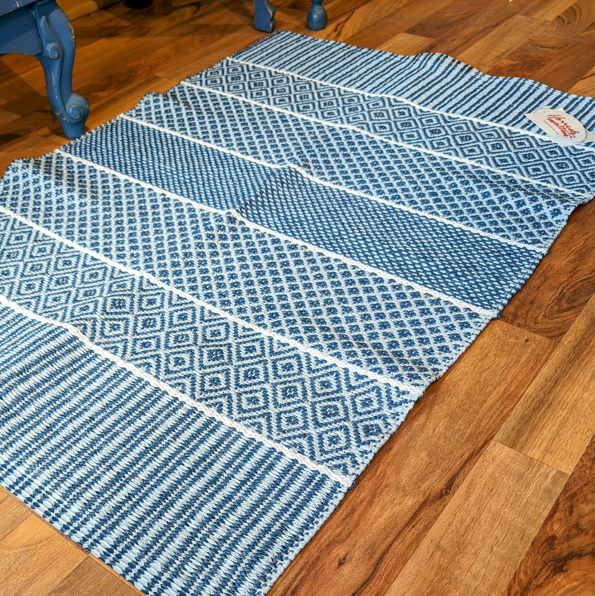 The Vinyl Rug: Horredsmattan - Alfie - Blue, featuring geometric patterns, is elegantly placed on a wooden floor beside a blue chair.