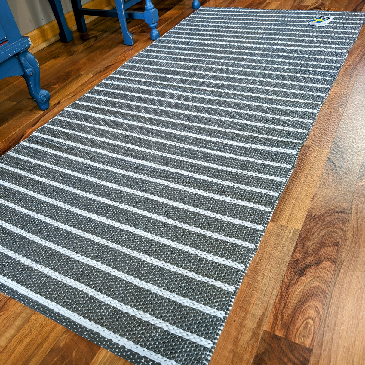 The dark gray Horredsmattan - Music vinyl rug rests on a wooden floor, complemented by nearby blue furniture.