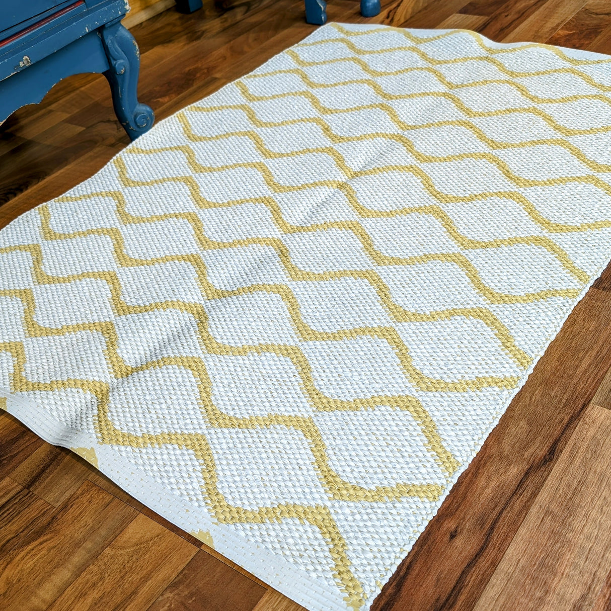 A Horredsmattan Vinyl Rug in yellow with a geometric diamond pattern is placed on a wooden floor next to blue furniture.