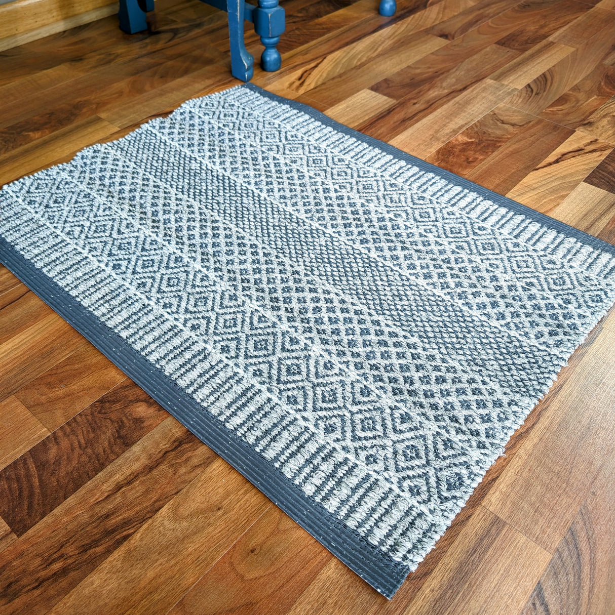 The Mixed Alice - Grey rug, crafted from cotton and vinyl, lies gracefully on the wooden floor, perfectly blending style with durability.