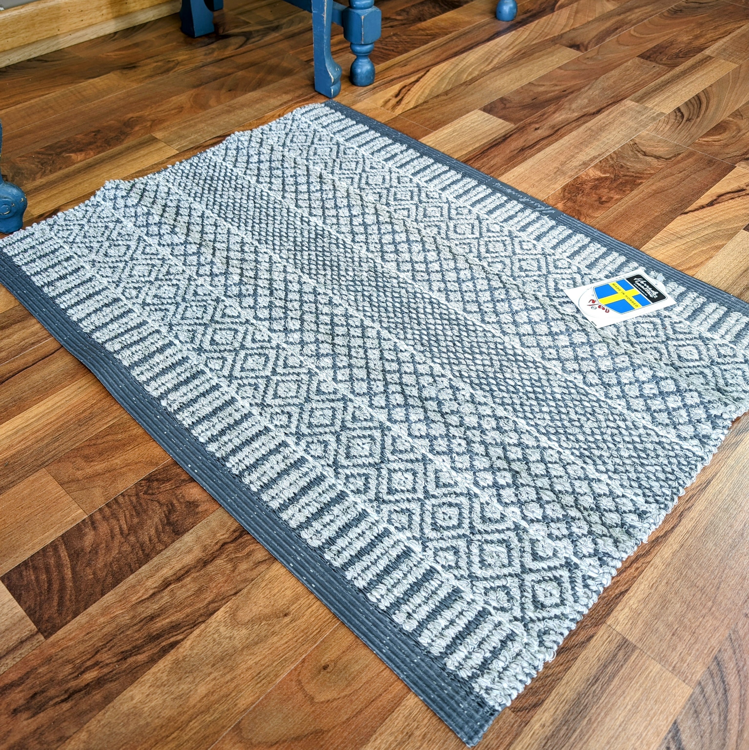 A small Rug: Mixed Alice - Grey, crafted from cotton and vinyl, graces the wooden floor, its Swedish-inspired design standing out beautifully.