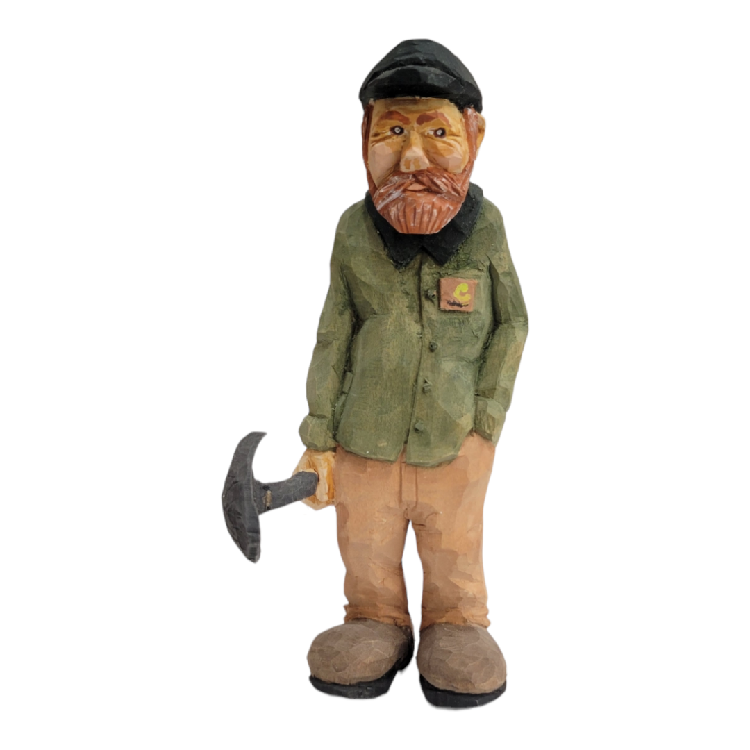 Hand-carved wooden figurine titled "Johannes with Shovel" by Bill Erickson, depicting a bearded man in a green shirt and cap, skillfully handling a pickaxe.