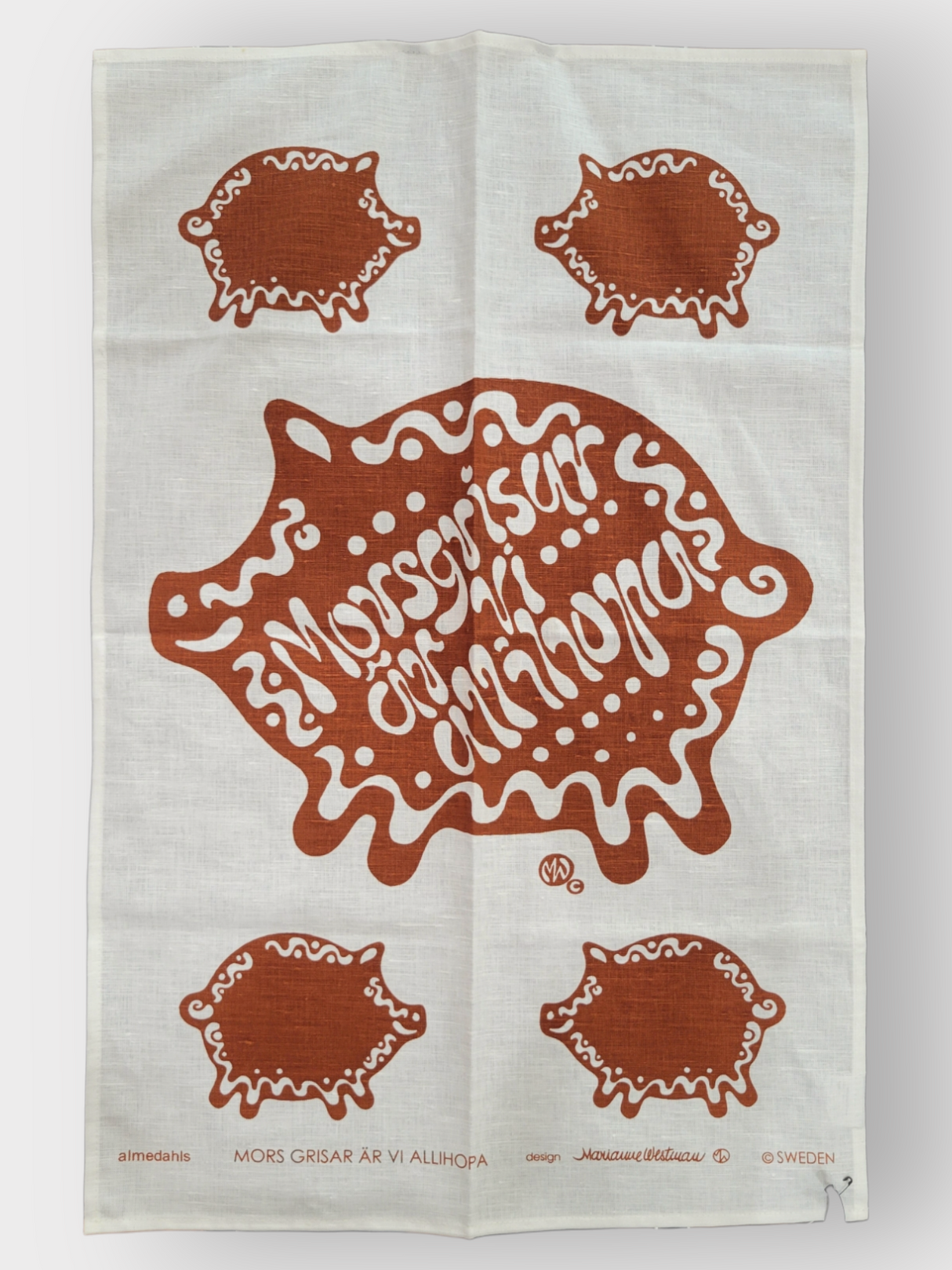 Introducing the Tea Towel: Pig – a charming kitchen accessory crafted from a linen and cotton blend. This delightful white towel features playful red pig designs and the Swedish phrase "Morsgrisar är vi allihopa," accompanied by smaller pig illustrations, adding a whimsical touch to any culinary space.