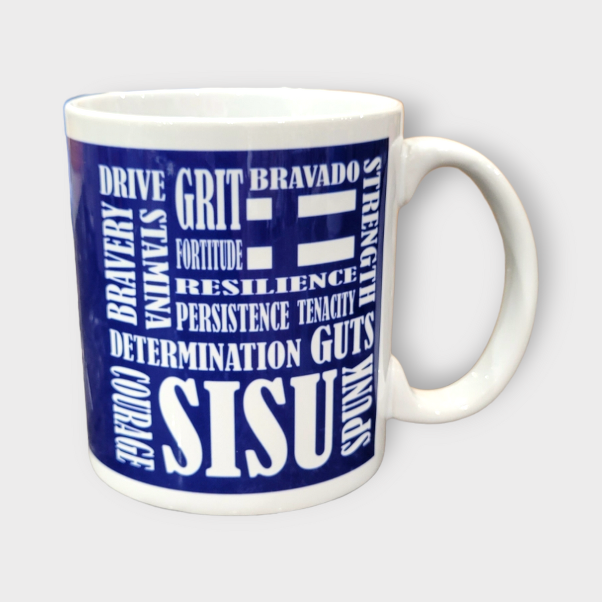 The Coffee Mug: SISU Scramble (11oz) features a blue background and bold white text with motivational words like GRIT, BRAVERY, STRENGTH, and COURAGE. This Finnish-inspired ceramic mug inspires you with every sip.