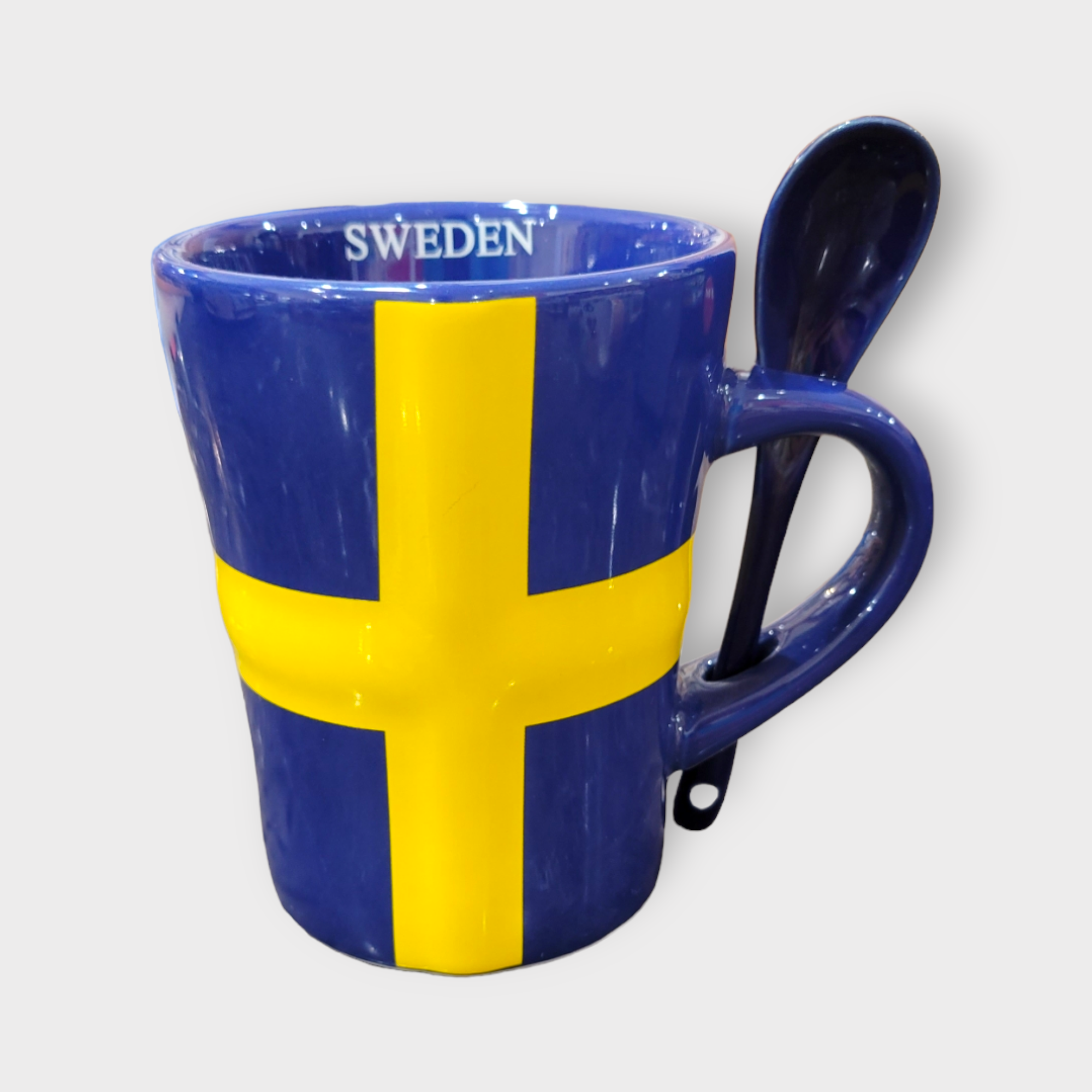 The "Sweden" Flag with Spoon Latte Style Mug (12oz) showcases the distinctive Swedish flag colors, featuring a blue base and a yellow cross. The word "Sweden" is gracefully inscribed on the rim. A coordinating blue spoon elegantly fits into the handle, enhancing its design. This mug is both dishwasher and microwave safe for added convenience.