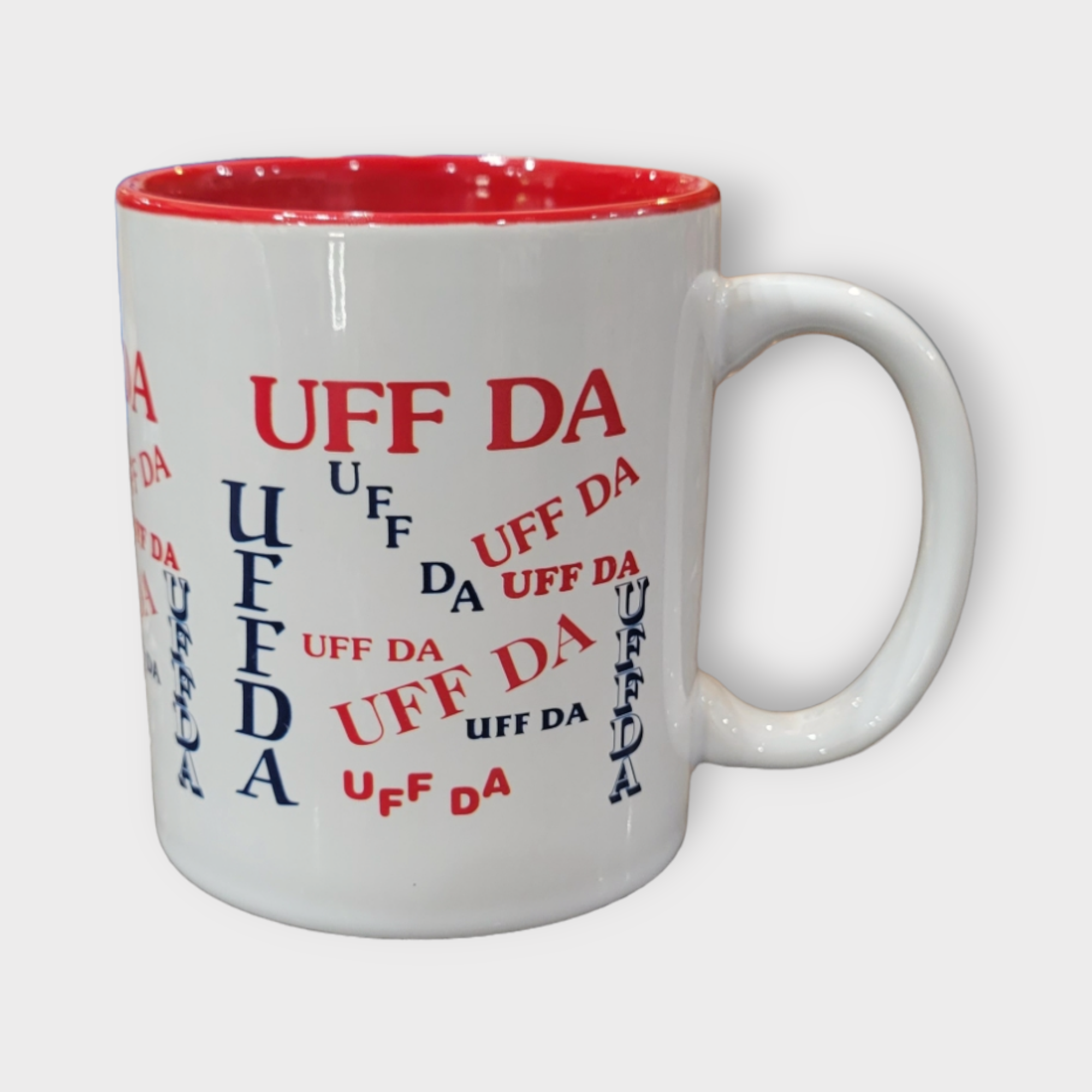 This 11oz mug features a white exterior and a red interior, highlighting the phrase "UFF DA" in varying sizes and orientations with red and blue text. Ideal for anyone celebrating their Nordic heritage, this Uff Da Mug pays homage to lively Scandinavian culture.