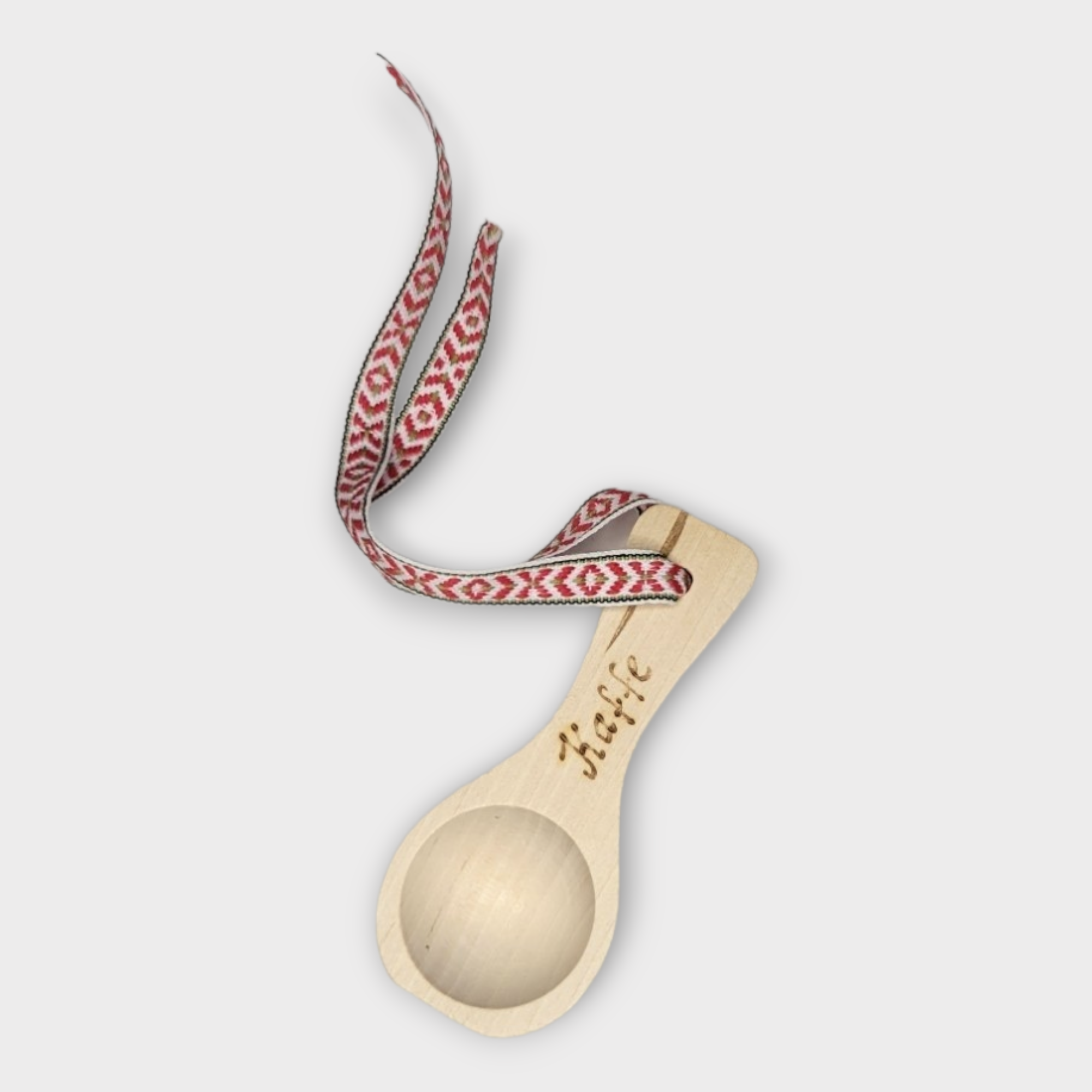 This charming coffee measuring spoon, known as the Kaffe Spoon, features a wooden design with a patterned red and white ribbon attached to the handle and is engraved with the word Häfle. Made in Sweden, it beautifully blends functionality with style.