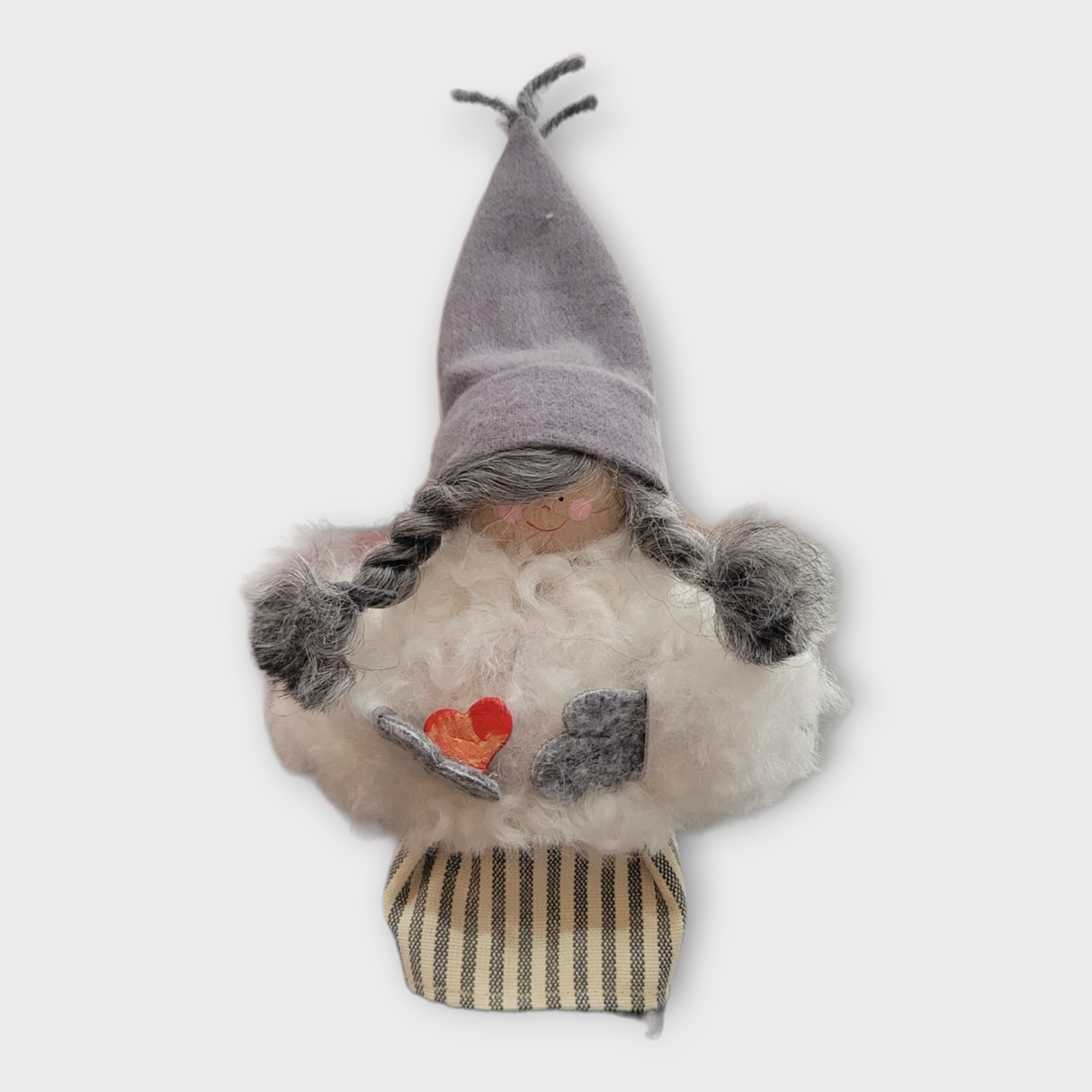 The Figurine: Sheepskin Tomte "Gnome" Holding a Heart sits against a white background—perfect as Swedish table decor with its handmade look, tall gray hat, fluffy beard, heart detail, and traditional Scandinavian style.