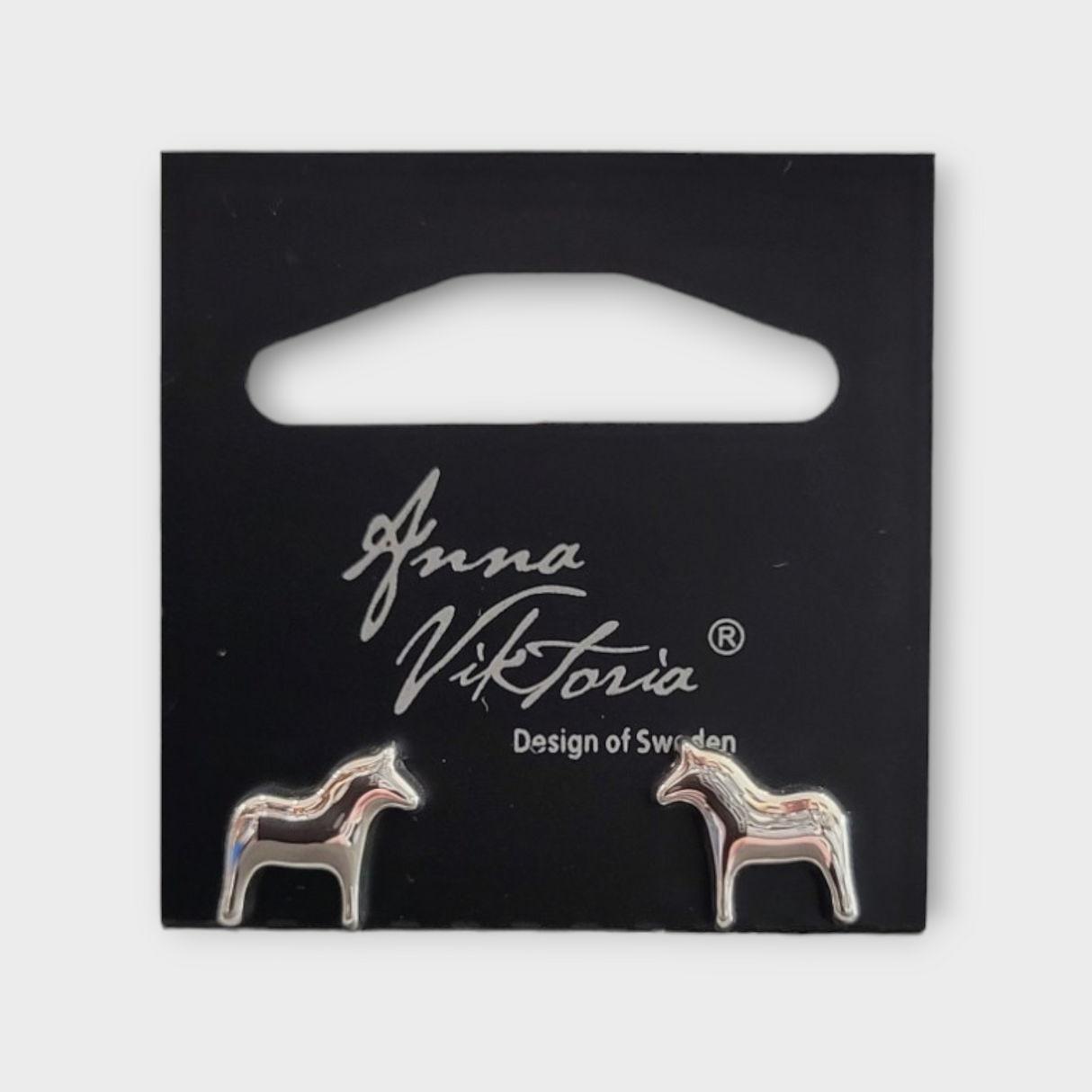 Silver Dala earrings shaped like horses, presented on a black card labeled Anna Viktoria, Design of Sweden, beautifully highlight the authentic charm of Scandinavian jewelry.