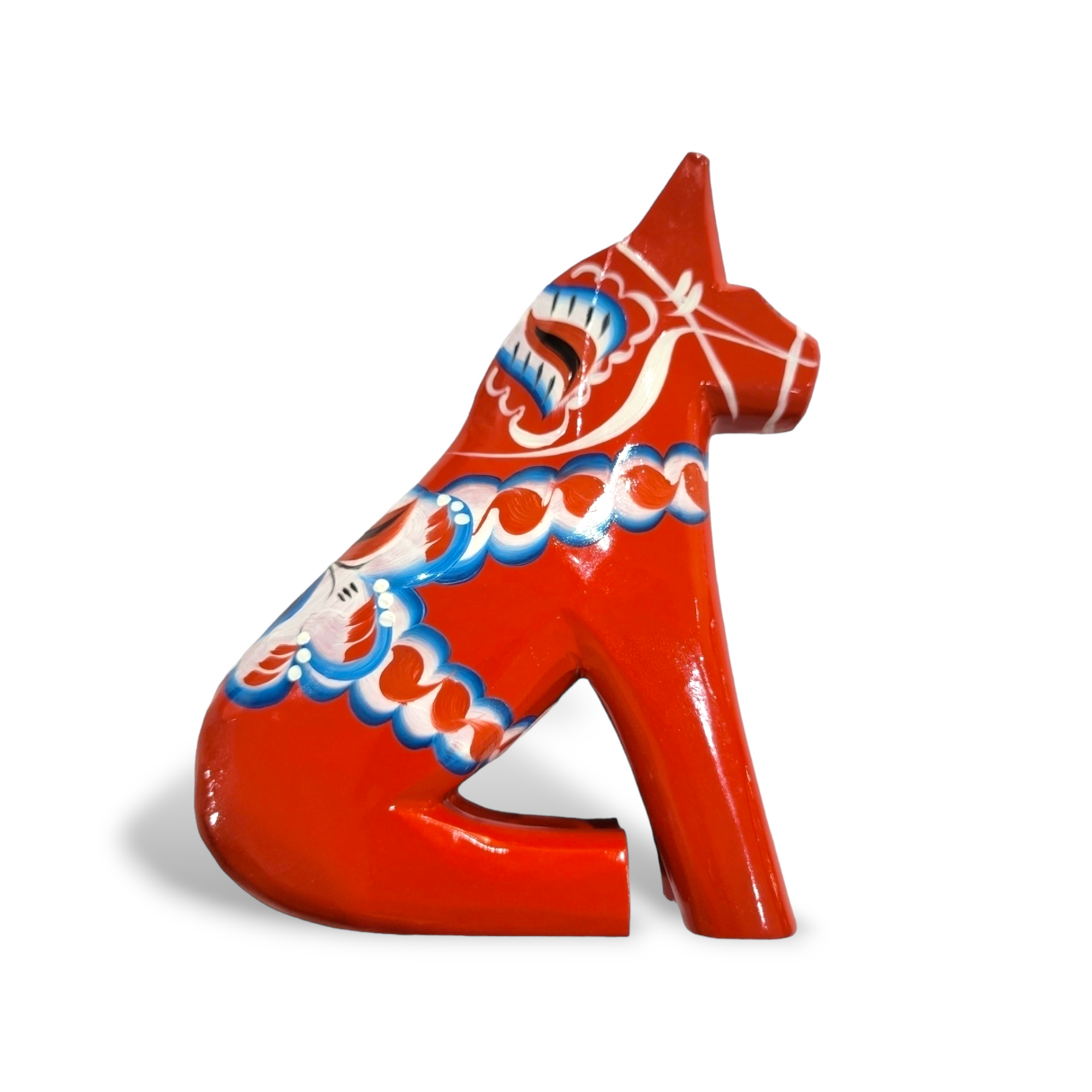 The Dala Horse: Sitting Red Dala Horse is a hand-carved Swedish figurine with blue, white, and green patterns, showcasing classic Swedish folk art. Photographed on a white background. Available in multiple sizes.