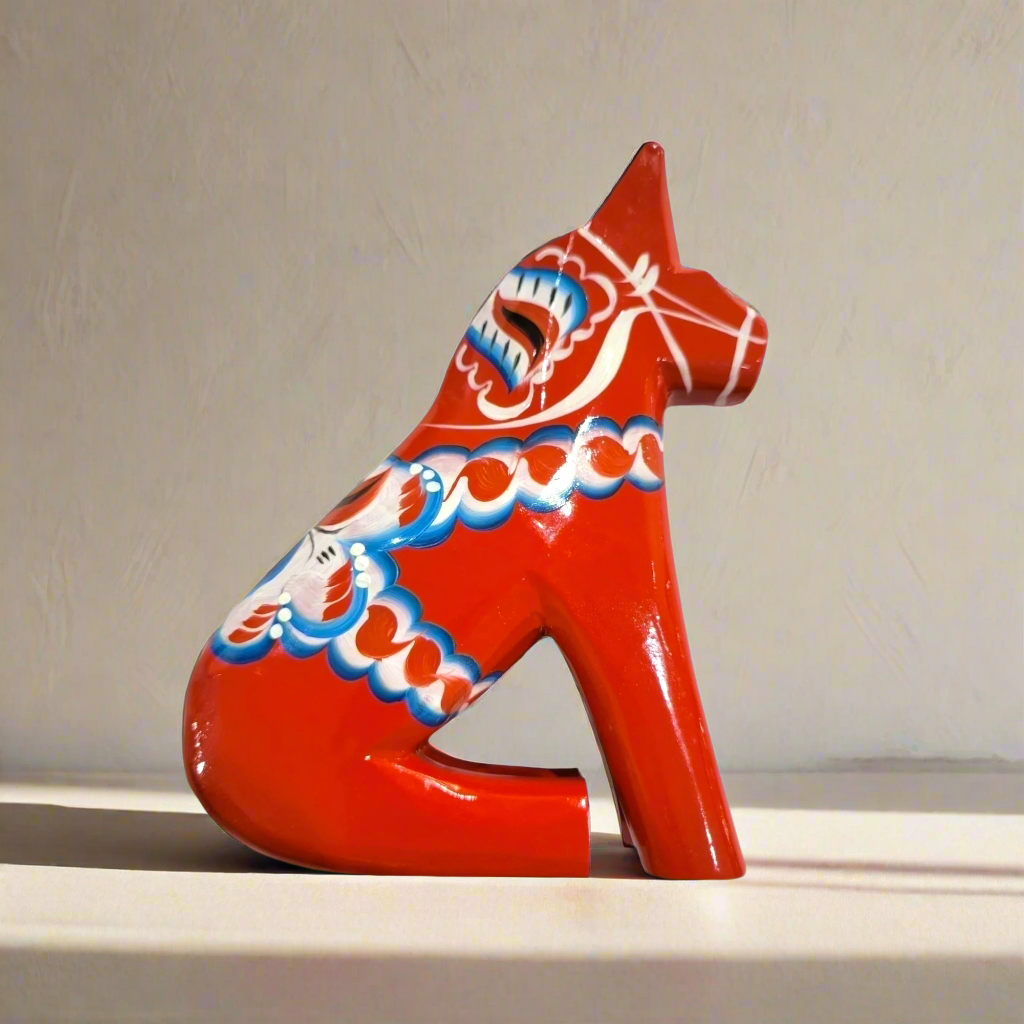The Dala Horse: Sitting Red Dala Horse – Hand-Carved Swedish Figurine (Multiple Sizes) is shown on a light surface, its red form decorated with white, blue, and green patterns, set against a simple background.