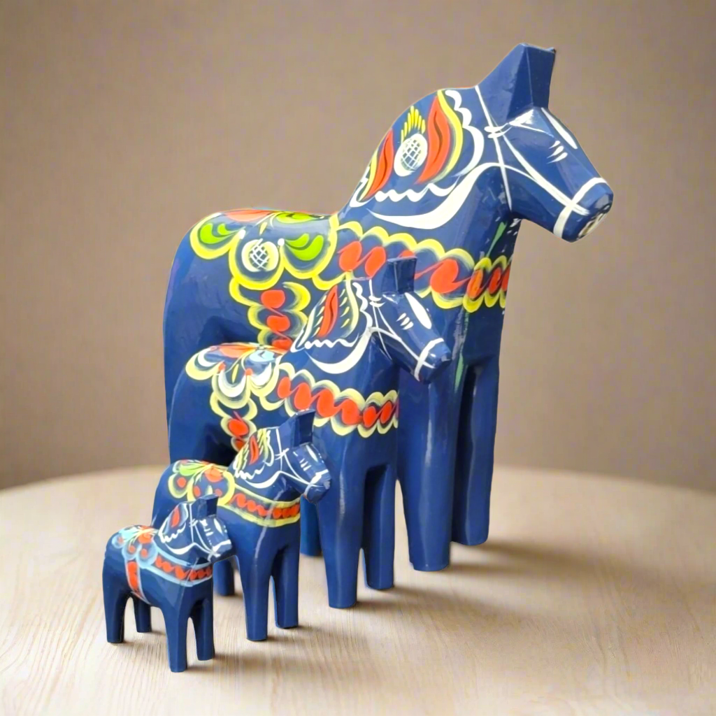Four dark blue, hand-carved Swedish Dala Horse figurines from the Dark Blue Dala Horse collection are arranged by size on a light wooden surface, highlighting colorful patterns and Scandinavian artistry.