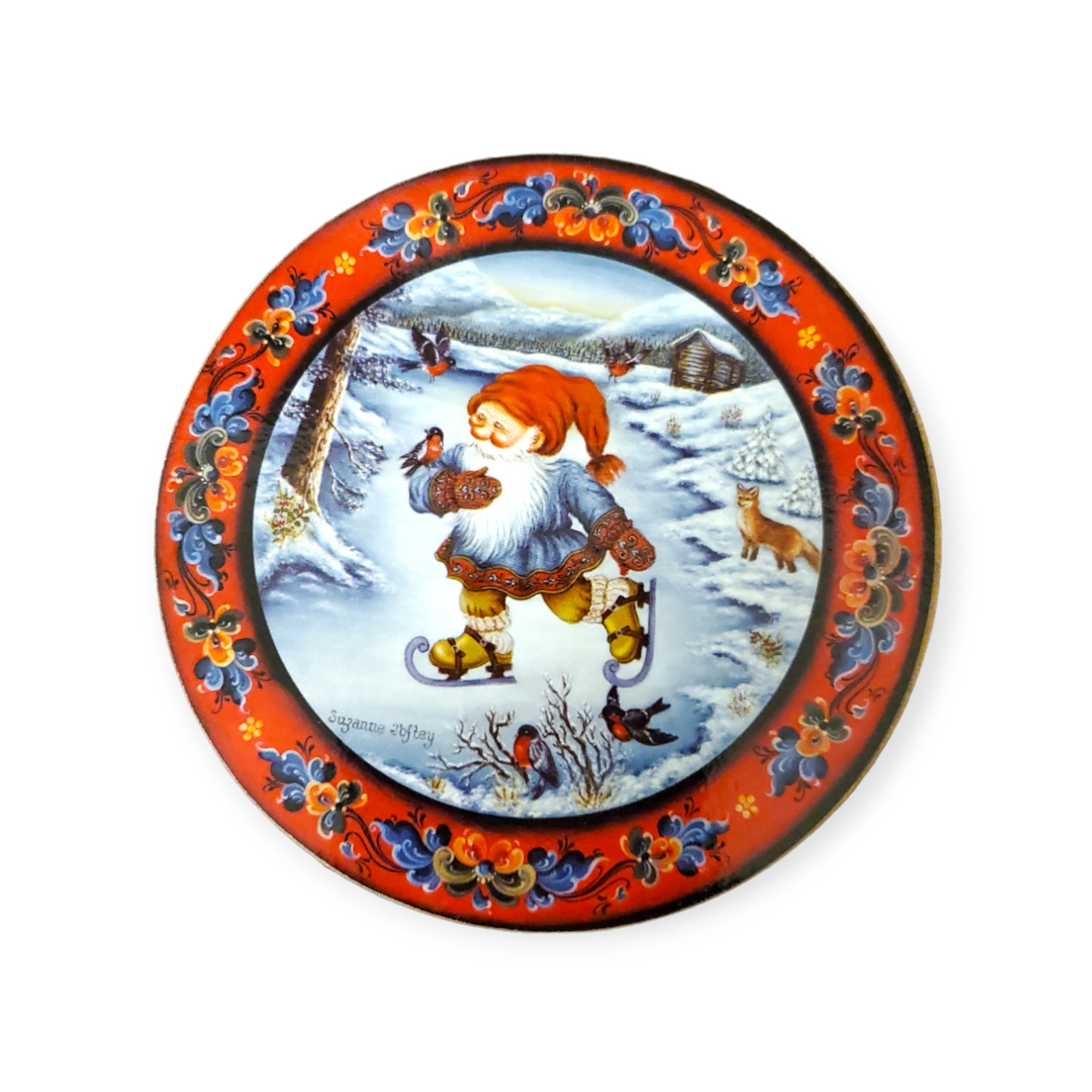 Round decorative plate featuring a festive scene with a gnome reminiscent of a Tomte in a snowy landscape, surrounded by birds, a rabbit, and a cabin. The ornate border displays red, blue, and floral patterns capturing the true essence of Julestemning. Part of the Coaster: Glassbrikker 6 pack collection.