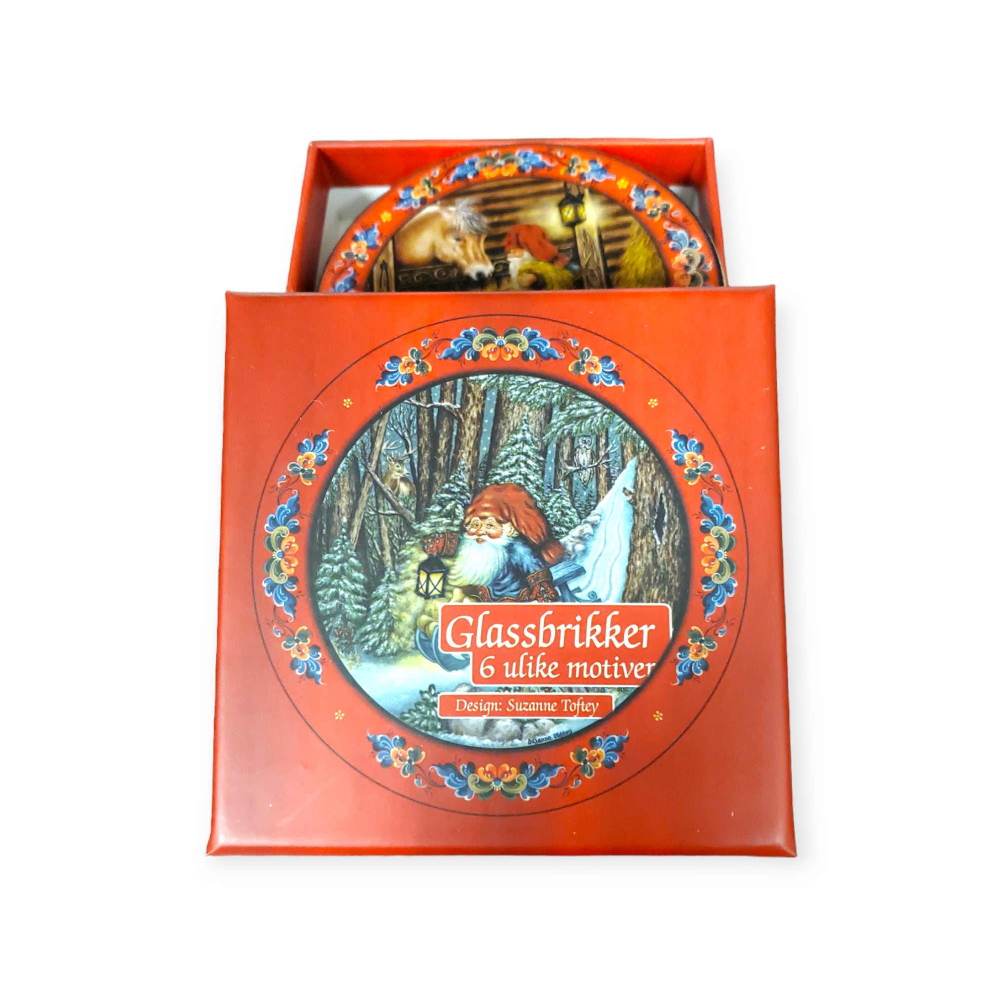 A festive coaster set called "Coaster: Glassbrikker 6 pack" captures the charm of a forest setting with enchanting designs by Suzanne Toftey, featuring a Santa figure. The label, "Glassbrikker, 6 ulike motiver," evokes true Julestemning with scenes reminiscent of a traditional Tomte.