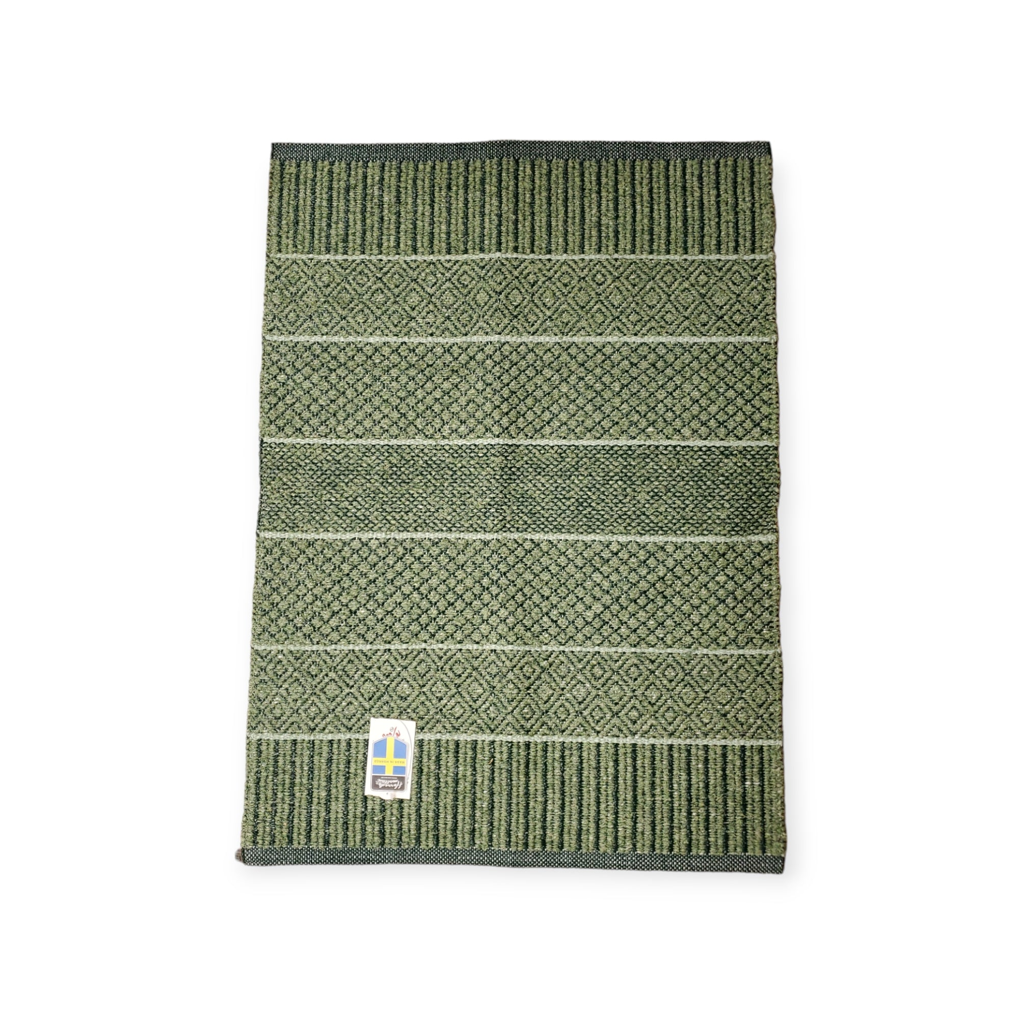 The Rug: Mixed Alice - Olive (Cotton & Vinyl) is showcased on a plain background, displaying its green patterned design with various textured stripes reminiscent of a Swedish vinyl woven rug. A small tag at the bottom corner emphasizes its durable, skid-resistant construction, perfect for versatile indoor and outdoor use.