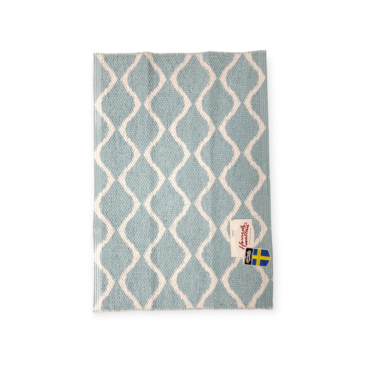 Presenting the Wave Blue rug, a reversible cloth with a durable Scandinavian design in a blue and white pattern, adorned with the Swedish flag label.