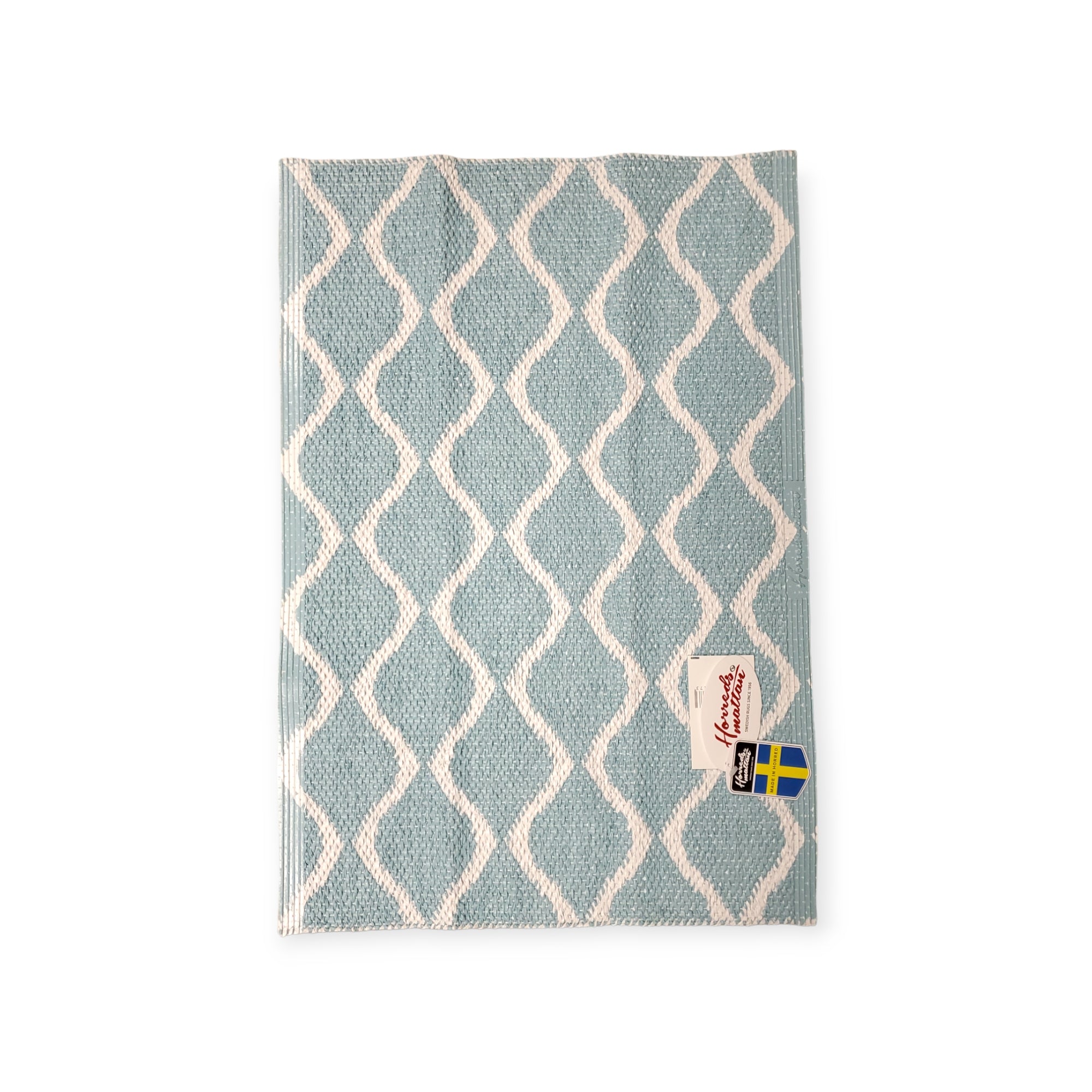 Presenting the Wave Blue rug, a reversible cloth with a durable Scandinavian design in a blue and white pattern, adorned with the Swedish flag label.