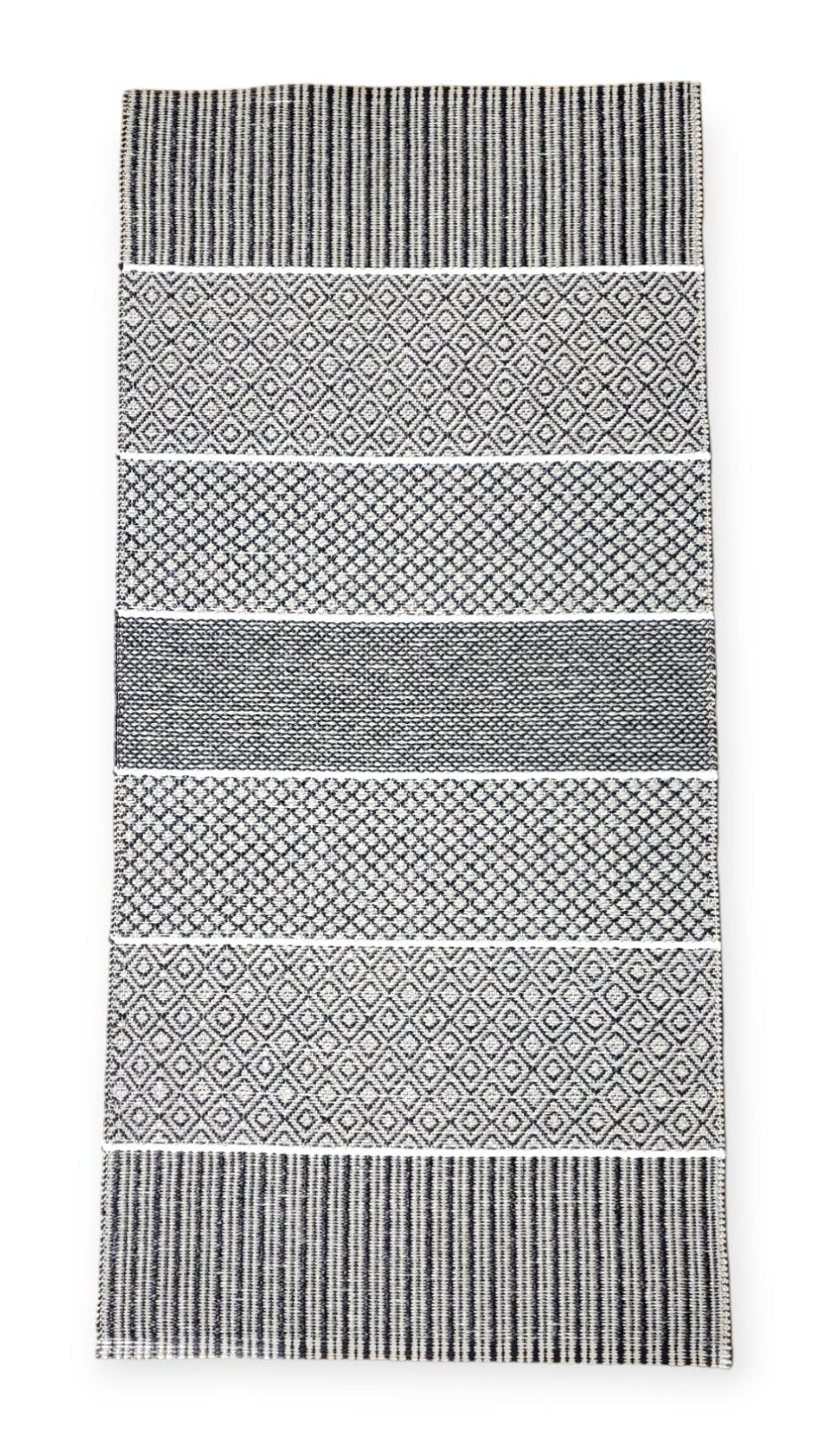 The Horredsmattan Alfie Graphite vinyl rug showcases a black and white pattern with alternating geometric stripes and diamond shapes, combining stylish design with sustainability thanks to its eco-friendly materials.