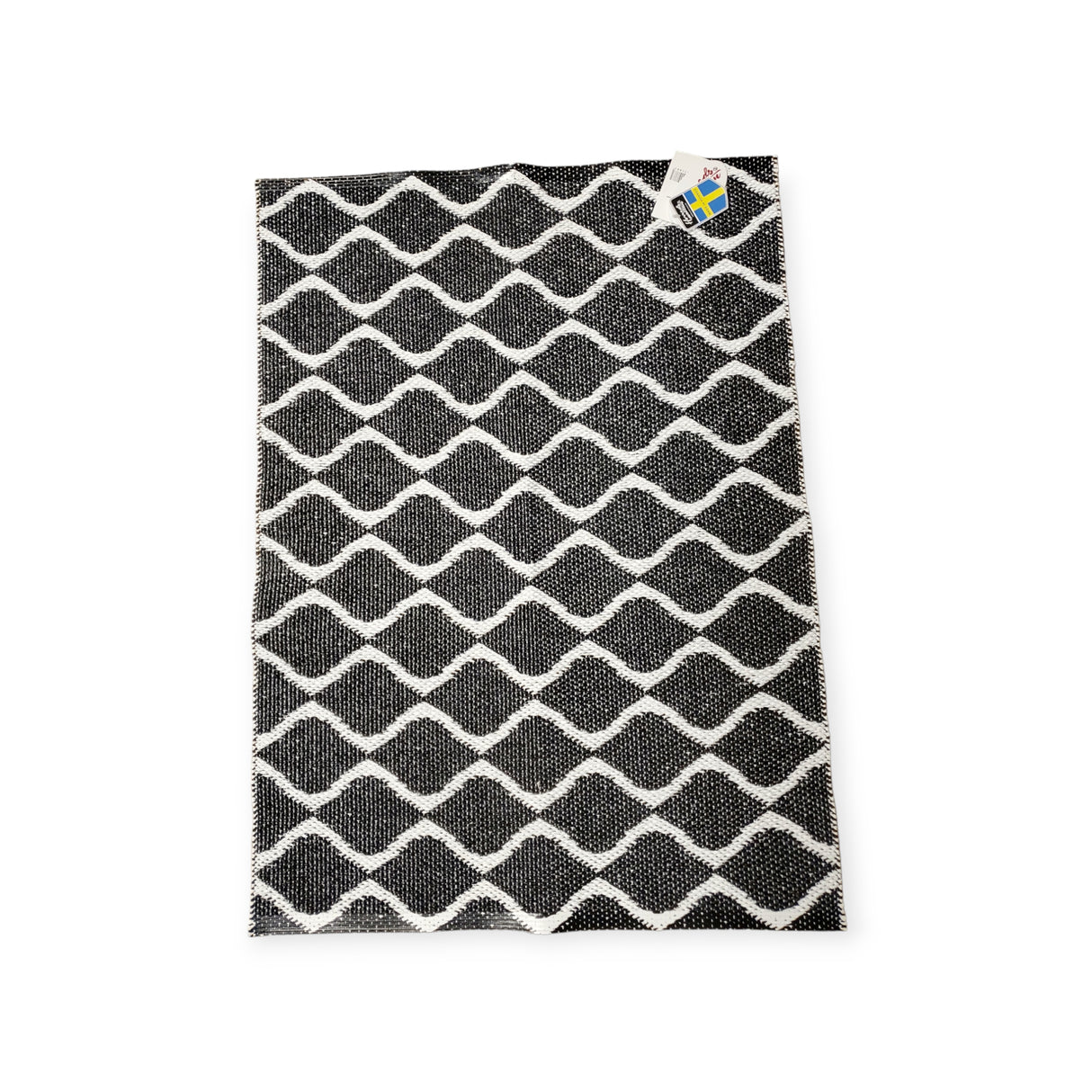 Introducing the Rug: Wave Black, a durable and long-lasting black and white Swedish Vinyl Rug showcasing a wavy grid pattern. This stylish piece includes a small label in the top right corner and offers a reversible design for versatile styling in any space.