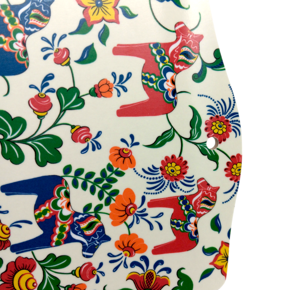 The Leksand Cream Serving Board features multi-color Swedish Dala horses and vibrant floral designs on a white background. This handcrafted ceramic piece from Sweden adds a charming touch to your table.