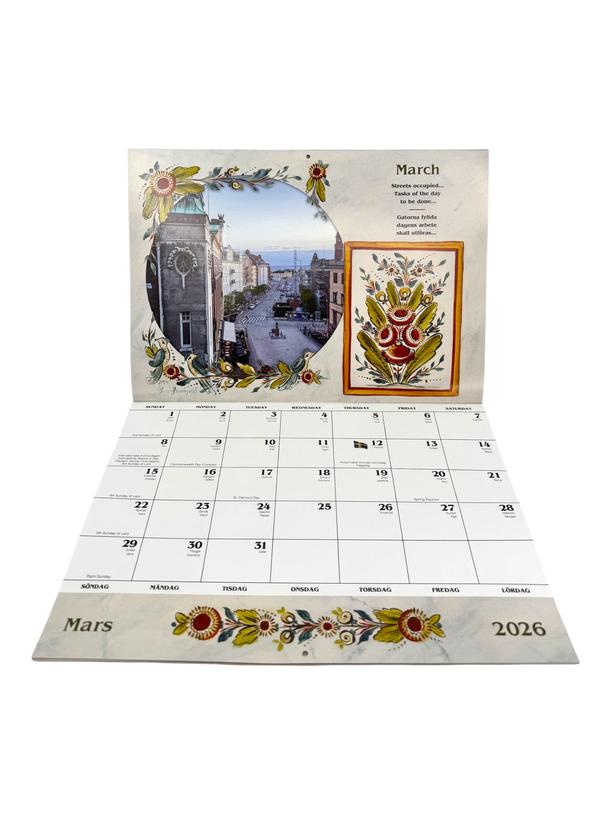 The Calendar: Sweden 2026 Wall Calendar – Visions & Verse of a Land and Its People is open to March, featuring Swedish day names, a floral border, city street photo, and folk art—celebrating Swedish culture.