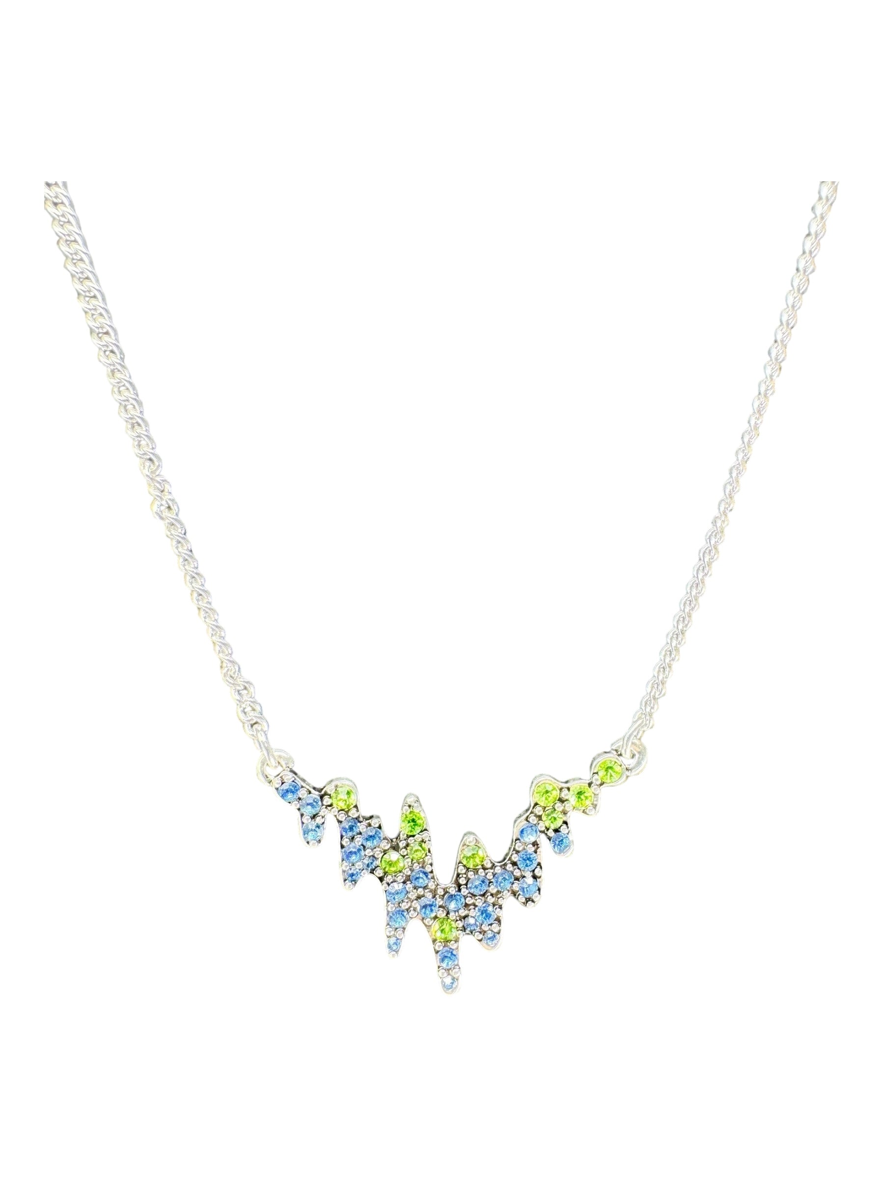 The Northern Lights A&C Oslo Norway Necklace features blue and green crystals in a jagged, abstract pendant, inspired by Norwegian jewelry and reminiscent of the captivating auroras. Silver plated.