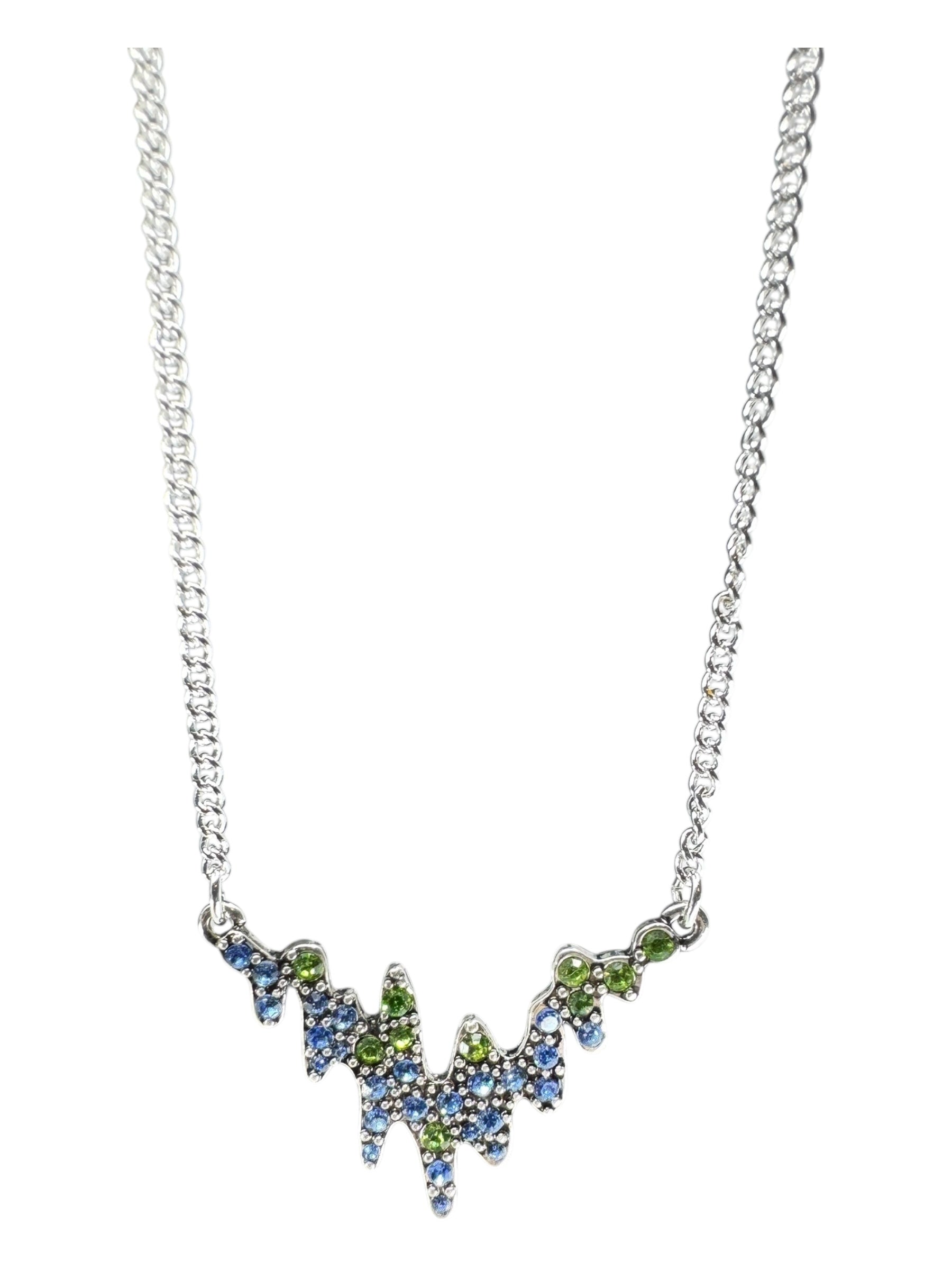 The Northern Lights Necklace by A&C Oslo features a jagged silver-plated pendant adorned with blue and green crystals, inspired by Norwegian jewelry.