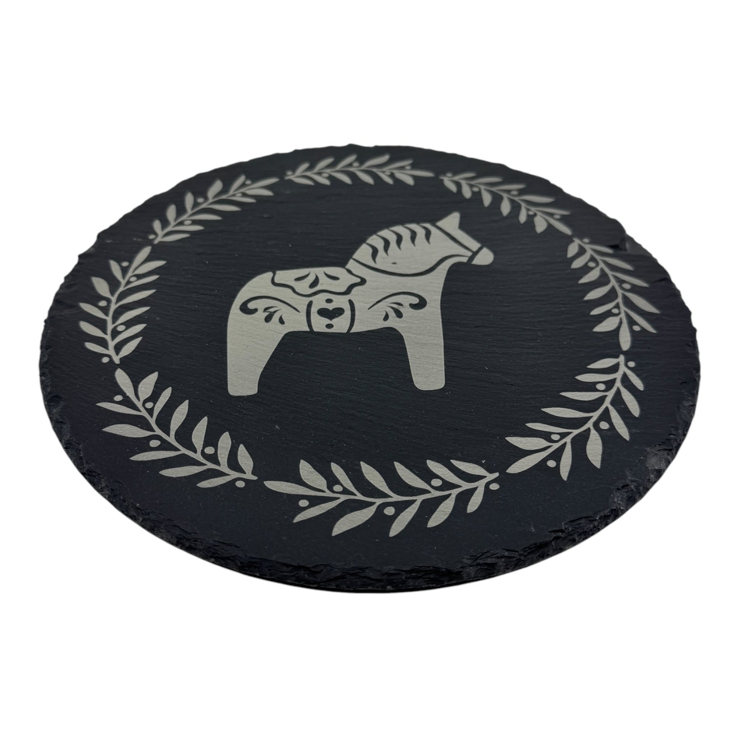 The 9.75 round slate trivet features a stylized Swedish Dala Horse at the center, encircled by a laurel leaf pattern inspired by Scandinavian design.
