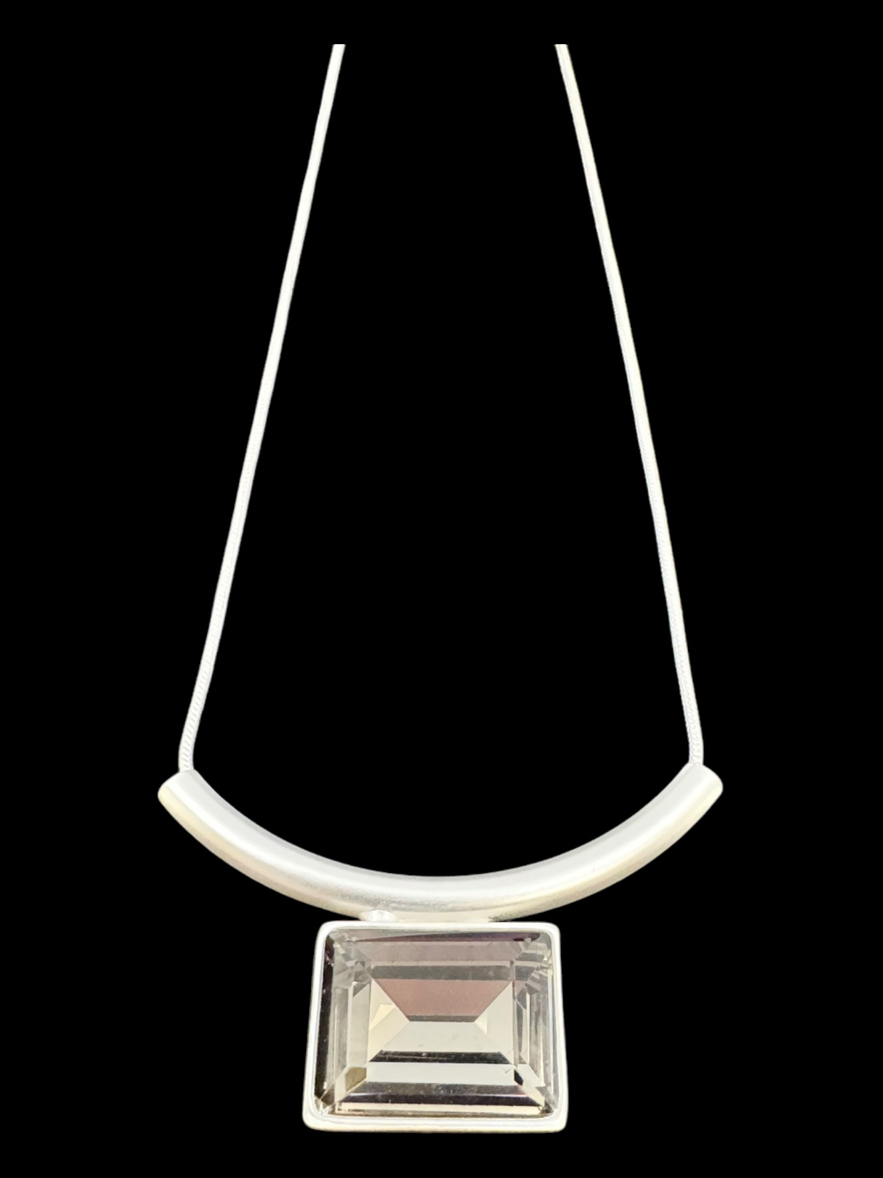 The Audrey Black Diamond Silver Plated Necklace by DANSK Copenhagen features a Nordic design with a clear rectangular pendant and curved white bar on a thin white cord, set against a black background. This elegant piece enhances any outfit with sophistication.