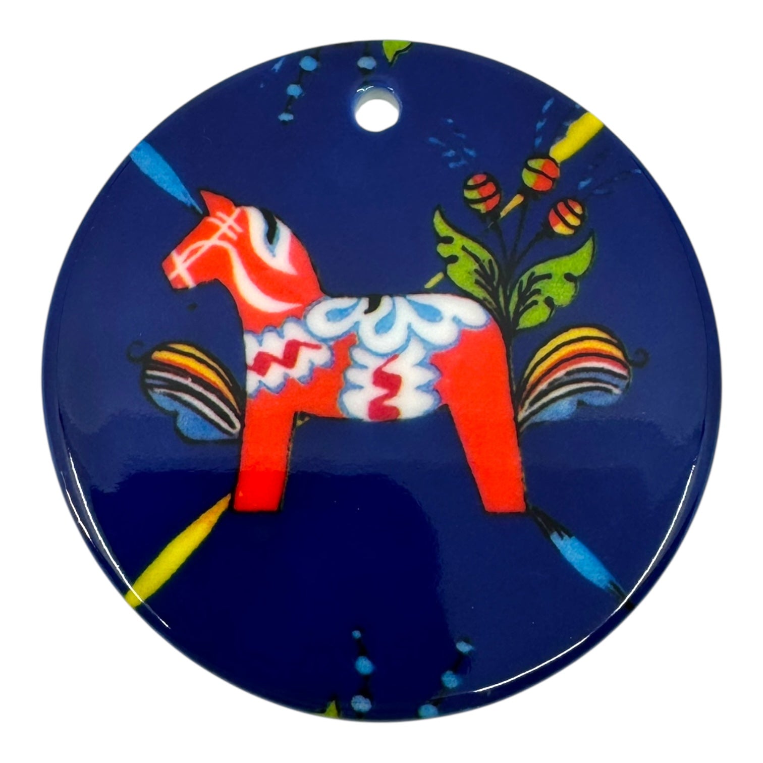 The Ornament: Dala Horse Ceramic 3 is a round blue porcelain ornament with a hole at the top, decorated with a red Dala Horse and yellow, green, and white floral patterns for Scandinavian charm.