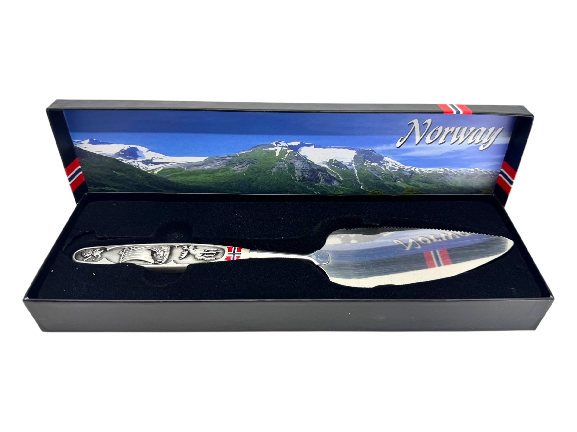 A Norwegian cheese slicer with a pewter handle featuring a Viking ship and moose image is displayed in a black box with a scenic mountain landscape, Norway on the lid, celebrating Scandinavian heritage.
