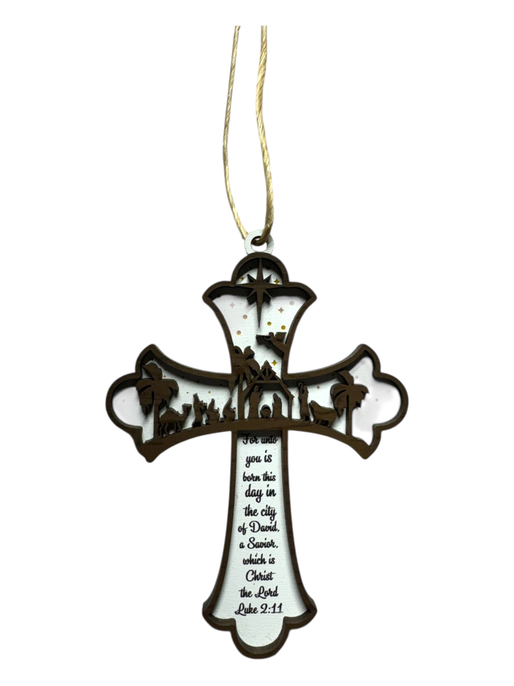 A white cross ornament with a brown border features a manger scene cutout, gold hanging string, and Luke 2:11 inscribed in black text.