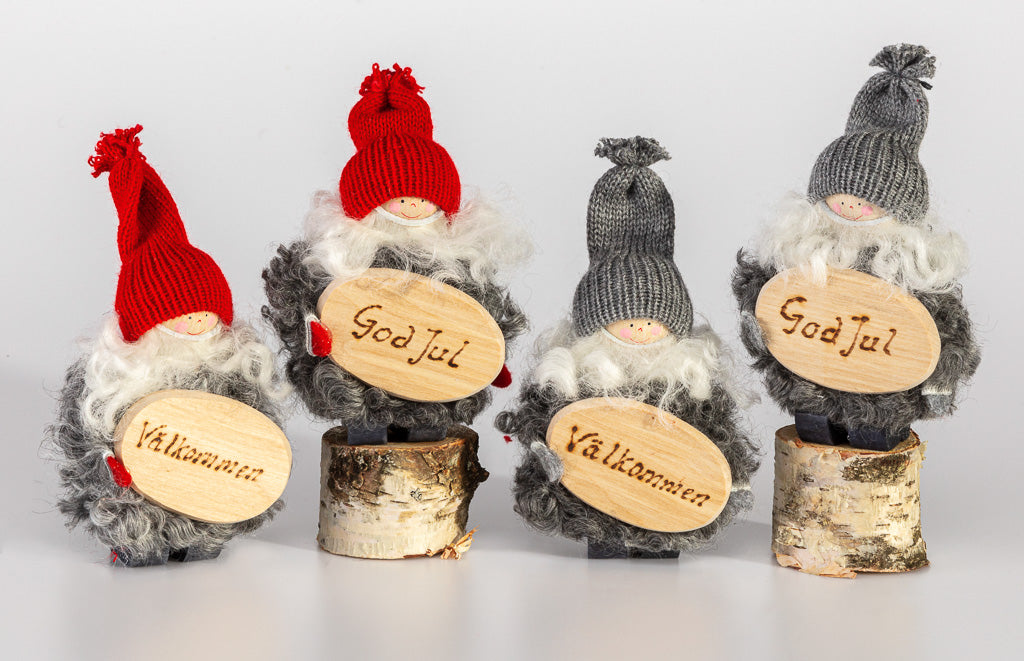 Four handcrafted "Tomte with God Jul Sign" figurines, featuring knitted caps and beards, stand proudly on birch log bases holding wooden signs that read God Jul and Välkommen. Made in Sweden.