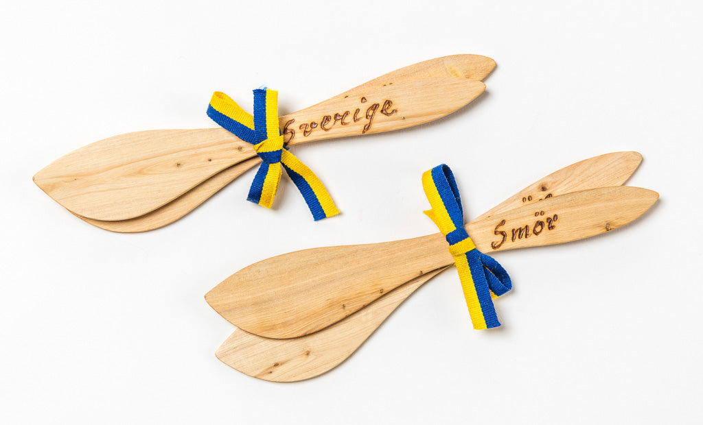 A set of two wooden butter spreaders, each engraved with "Sverige" and "Smör," adorned with blue and yellow ribbons that reflect the colors of the Swedish flag.