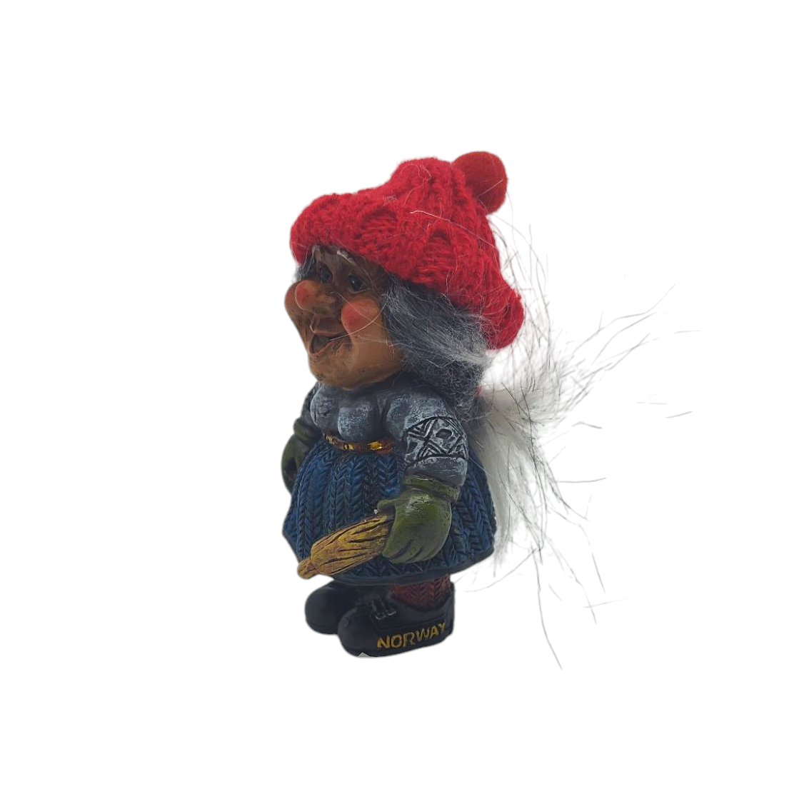 Side view of a smiling Nisse wife figurine, wearing a red knit hat and blue dress, holding a rolling pin, with Norway displayed near the base.
