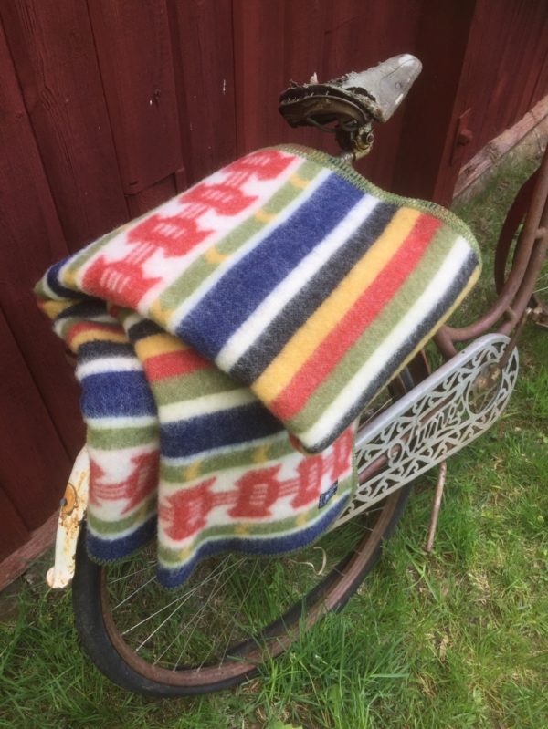 A Rattvik blanket made from 100% Norwegian lambs wool by Kerstin Landstrom, featuring traditional Swedish patterns, is draped over a vintage bicycle against a wooden fence.