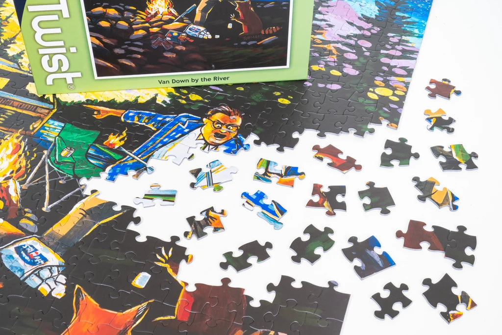Partially assembled 500 piece jigsaw puzzle with loose pieces, featuring a man in a blue shirt and glasses by a campfire next to a river.