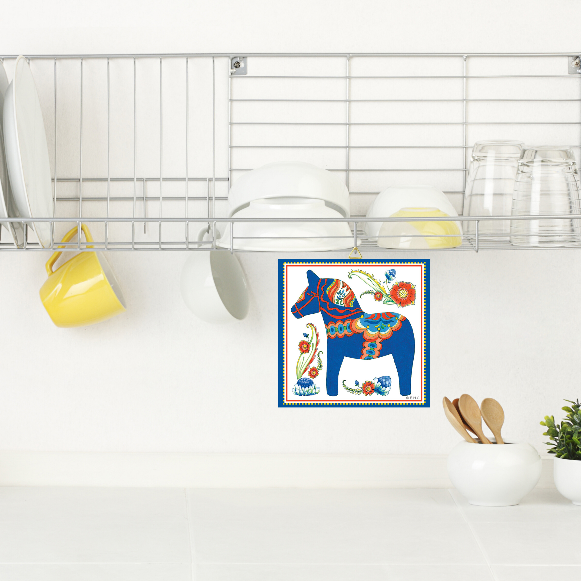 A kitchen scene with white dishes and yellow mugs on a drying rack above the counter; the "Tile: Blue Swedish Dala Horse Wall Tile Design 6x6" decorates the wall.