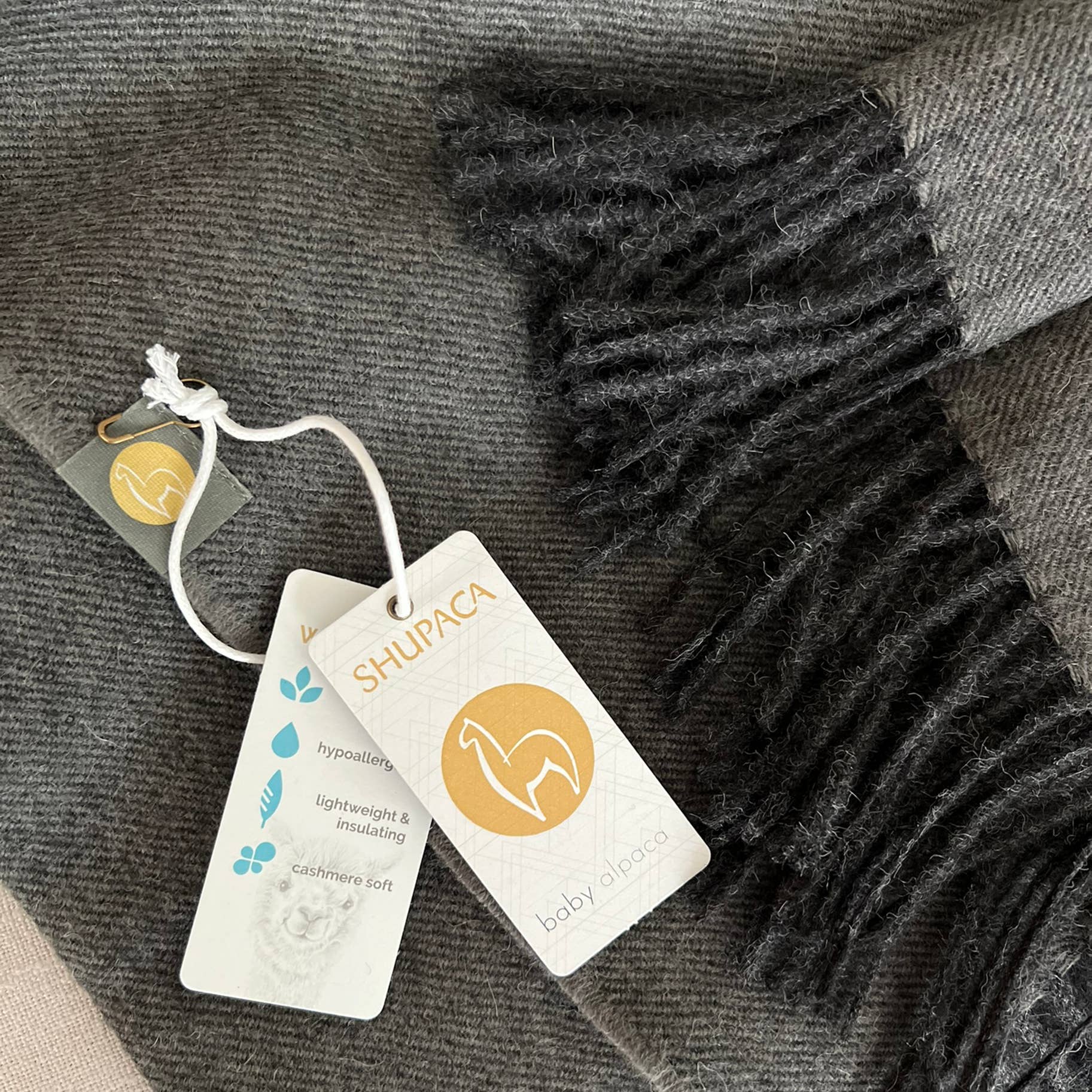 Introducing the Scarf: 100% Baby Alpaca Scarf - Carbon, a luxurious piece complete with tags that highlights its baby alpaca origins and exceptional features like being hypoallergenic, lightweight, and insulating.