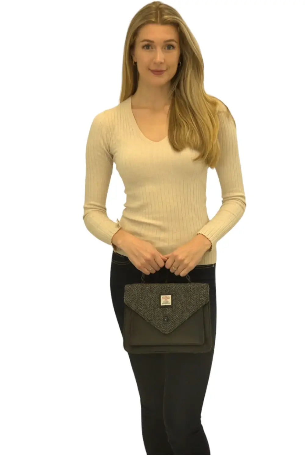 A woman in a beige long-sleeve top and black pants stands against a plain white background, holding the Harris Tweed Large Satchel - Grey.