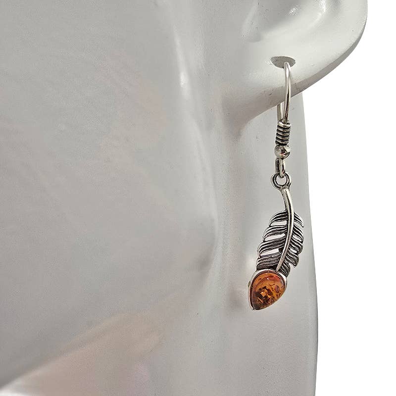 A close-up of Earrings: Amber Sterling Silver Feather Earrings On Hooks, featuring an amber-colored stone in a sterling silver feather design—ideal for fans of elegant amber jewelry.